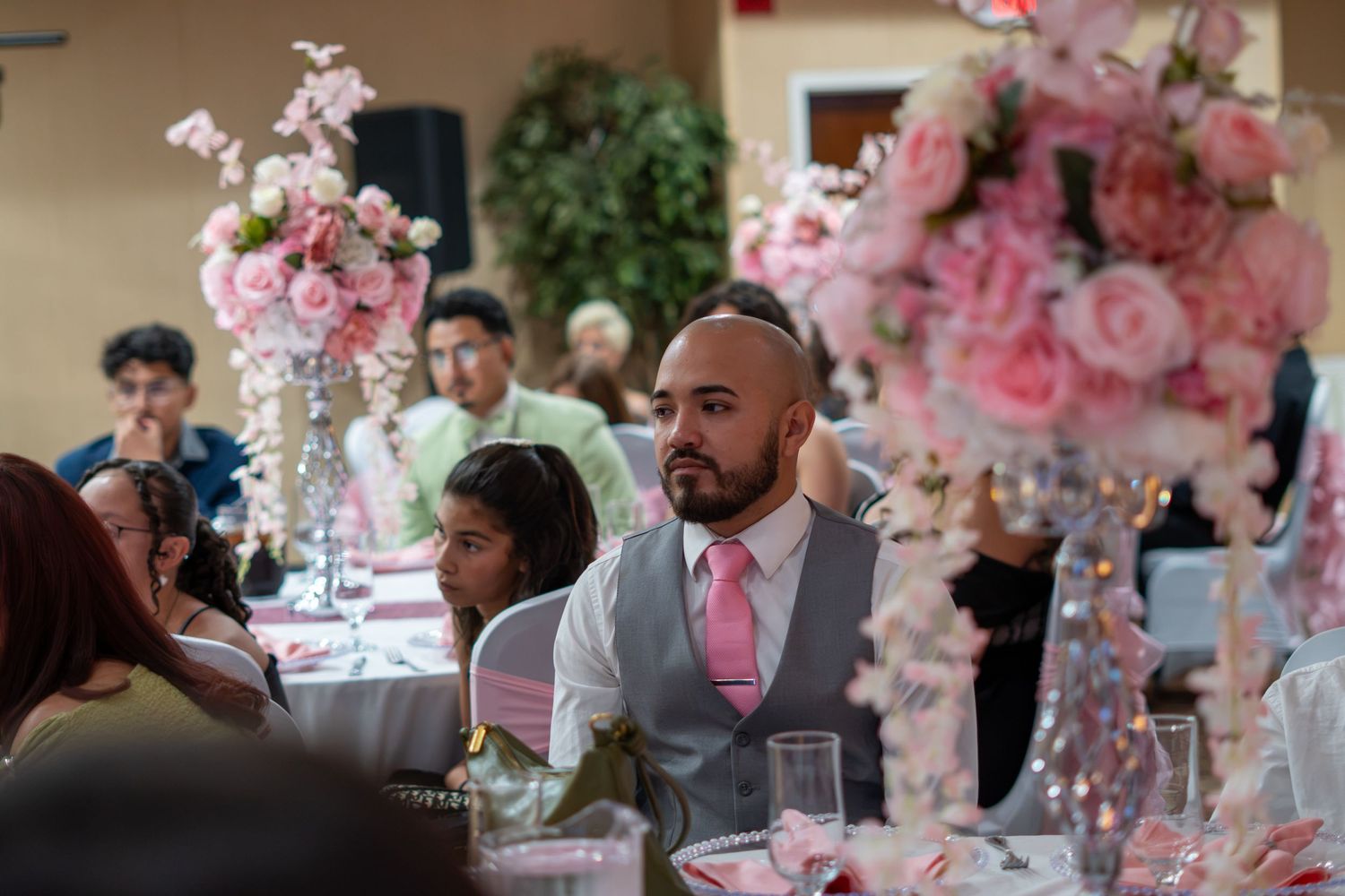 Man in vest and pink tie seated at elegantly decorated wedding reception table with pink floral centerpieces. Sweet 16!