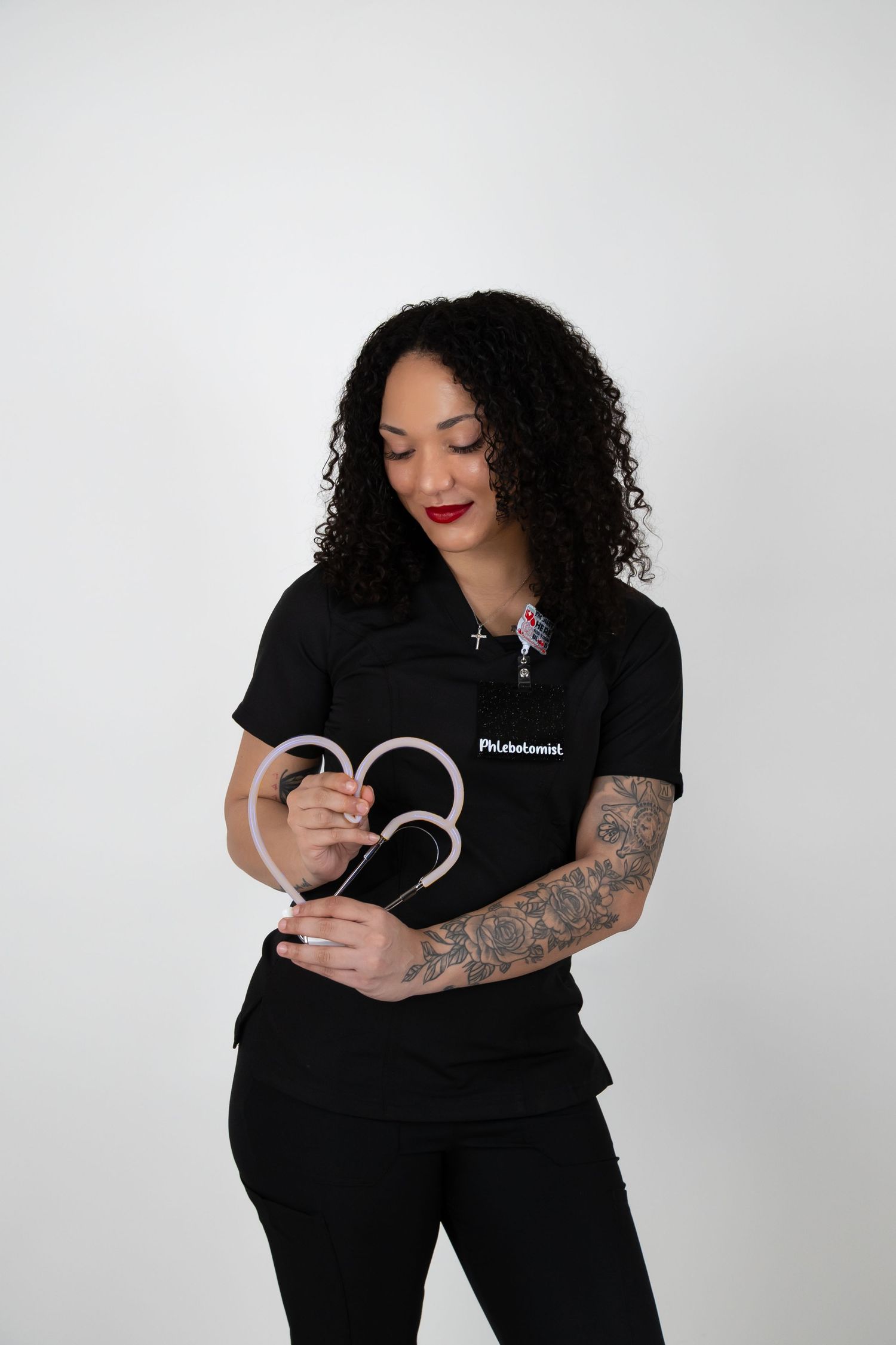Female phlebotomist in black scrubs holding medical tubing in a professional portrait.