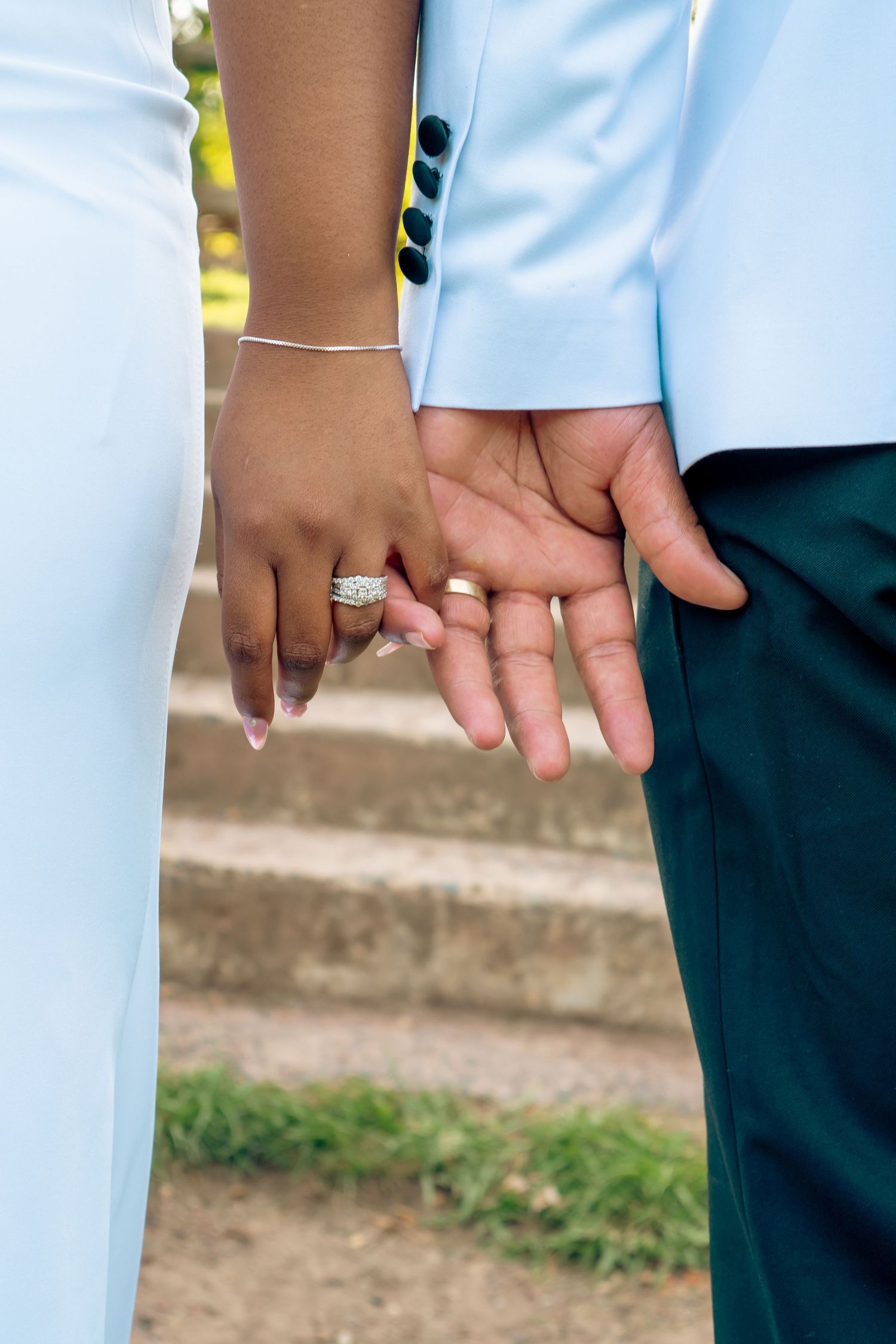 Close-up of bride and groom holding hands displaying diamond wedding rings in matching light blue wedding attire.