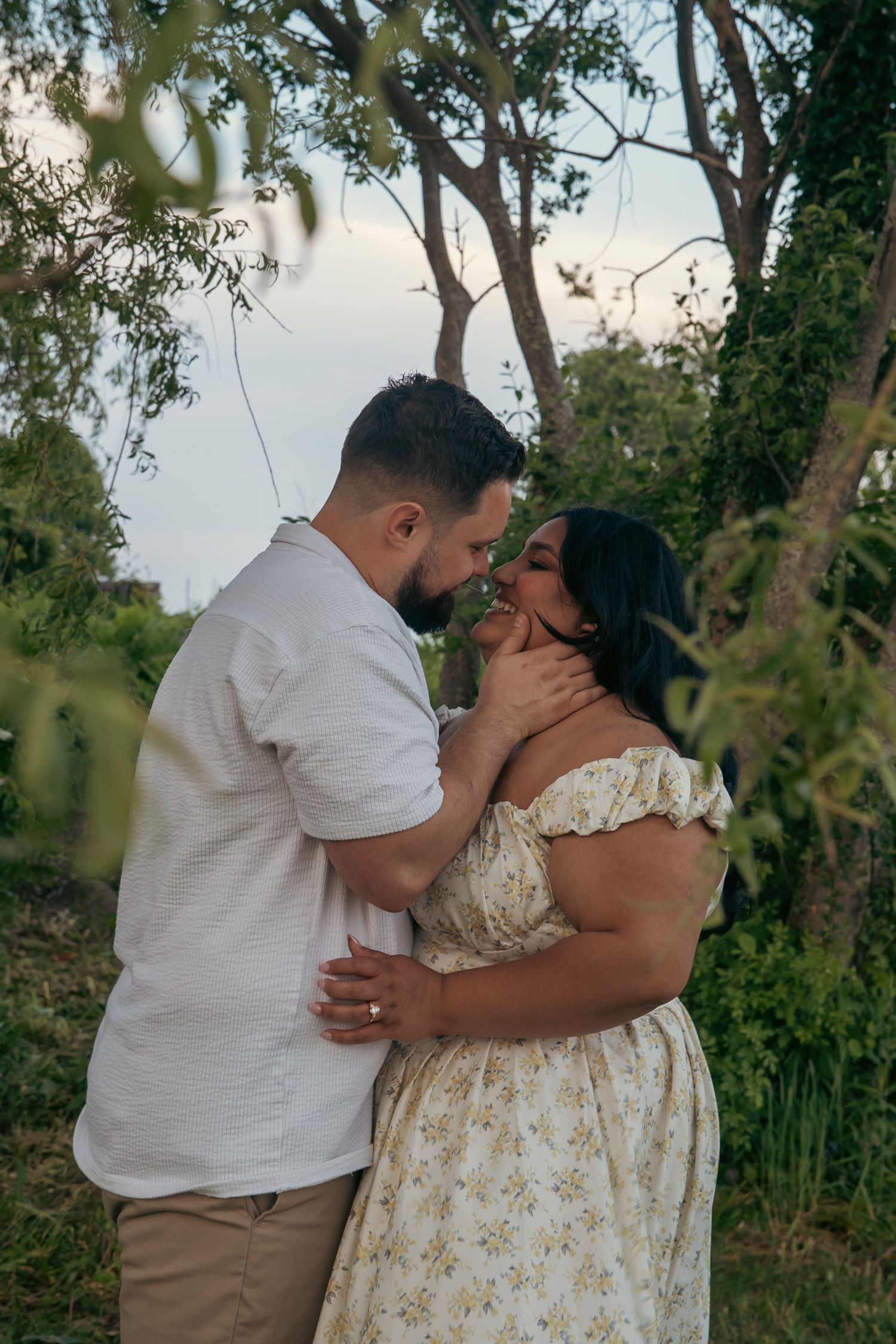 A couple shares a tender moment in a lush garden, the man gently holding the woman's face as they lean in close.