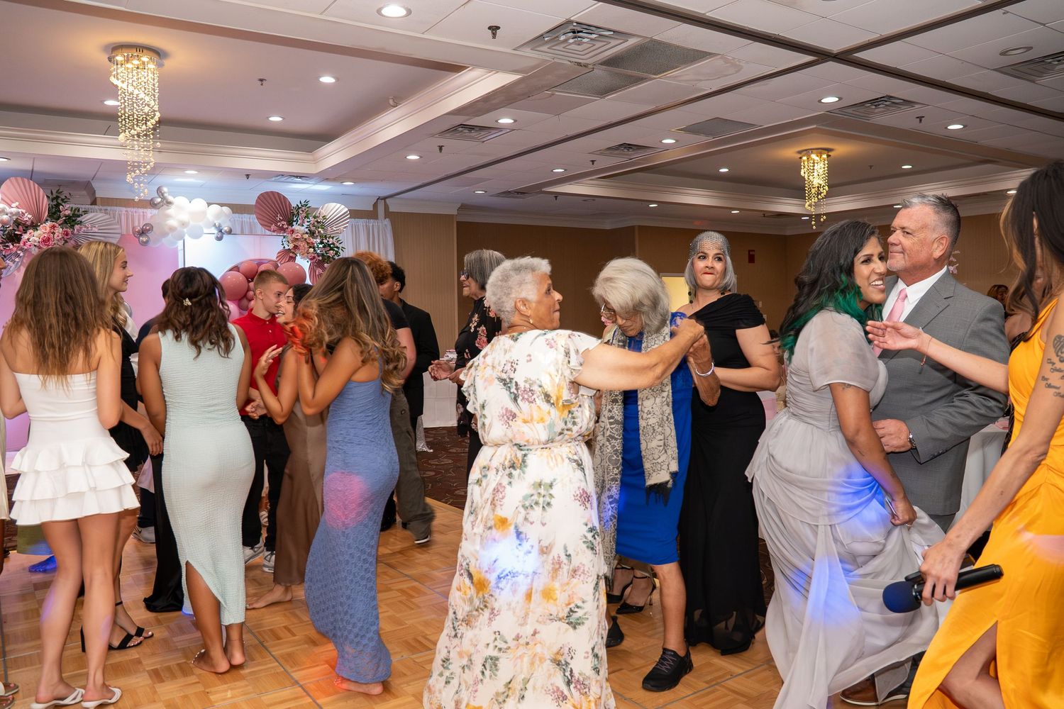 Guests dancing together at a festive indoor party celebration in a decorated banquet hall. Sweet 16!
