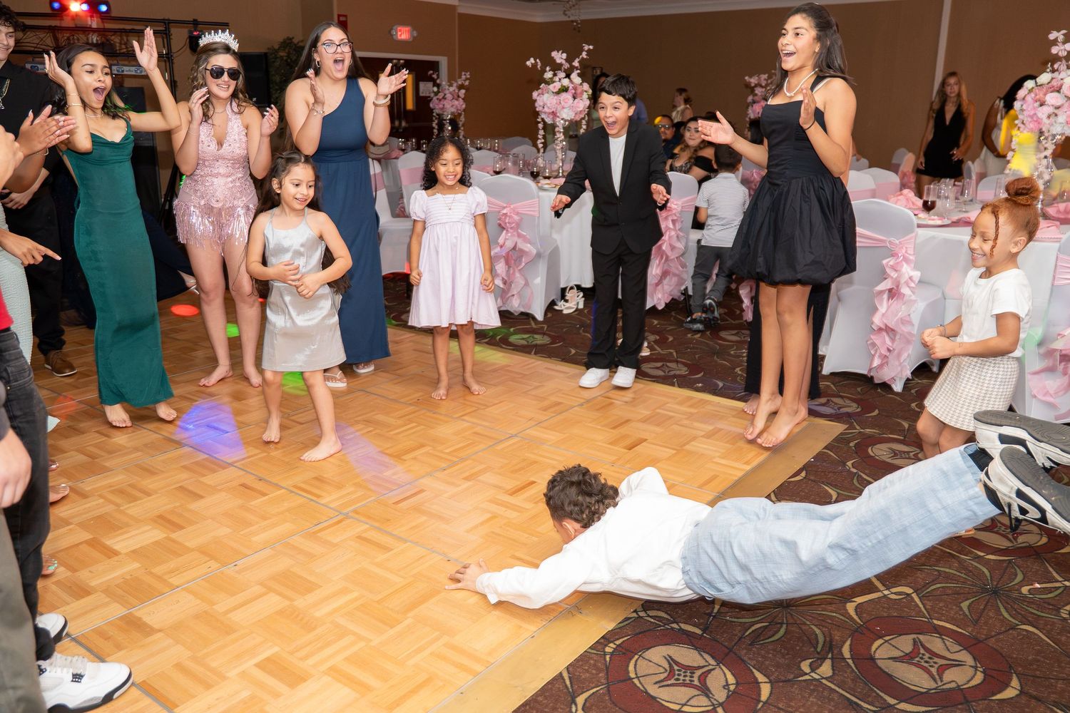 Excited guests cheer as a boy does a dramatic dance move on the floor at a quinceañera. Sweet 16!