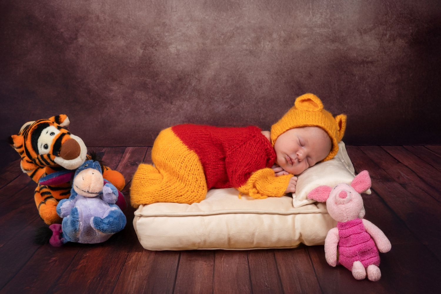 Sleeping newborn baby dressed in Winnie the Pooh outfit surrounded by stuffed animals.
