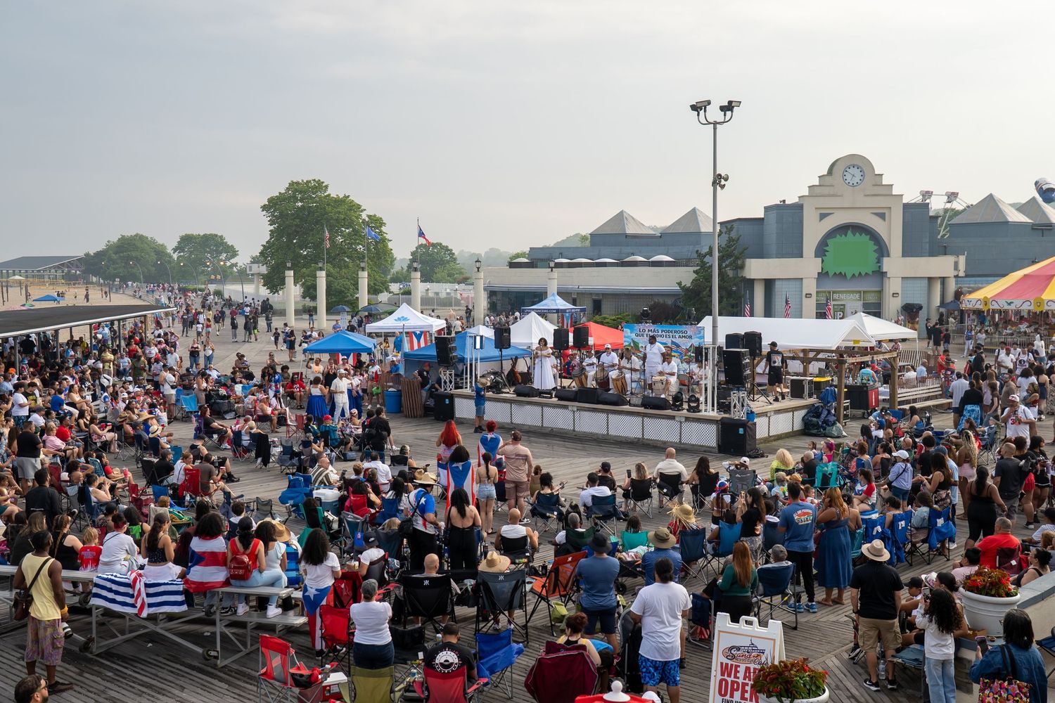 Large outdoor festival crowd gathered near a waterfront stage with tents and a green-domed building in the background.