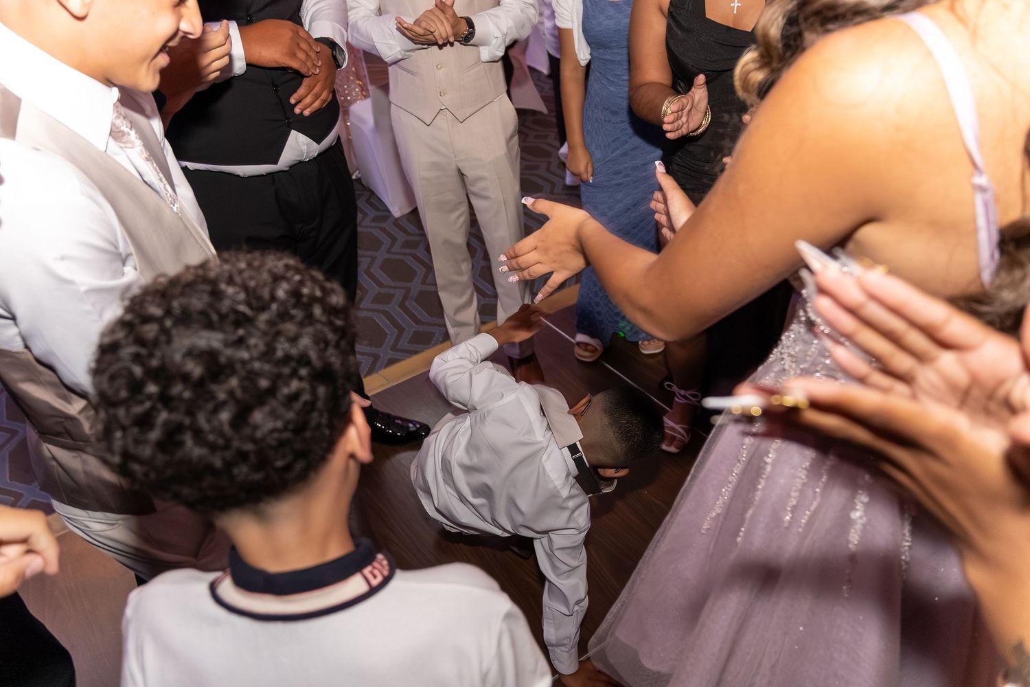 A young boy doing the limbo on a crowded dance floor surrounded by guests at a formal celebration. Sweet 16!