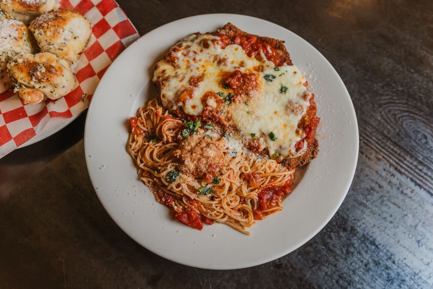 Chicken parmesan served over spaghetti with marinara sauce, topped with melted mozzarella cheese on a white plate.