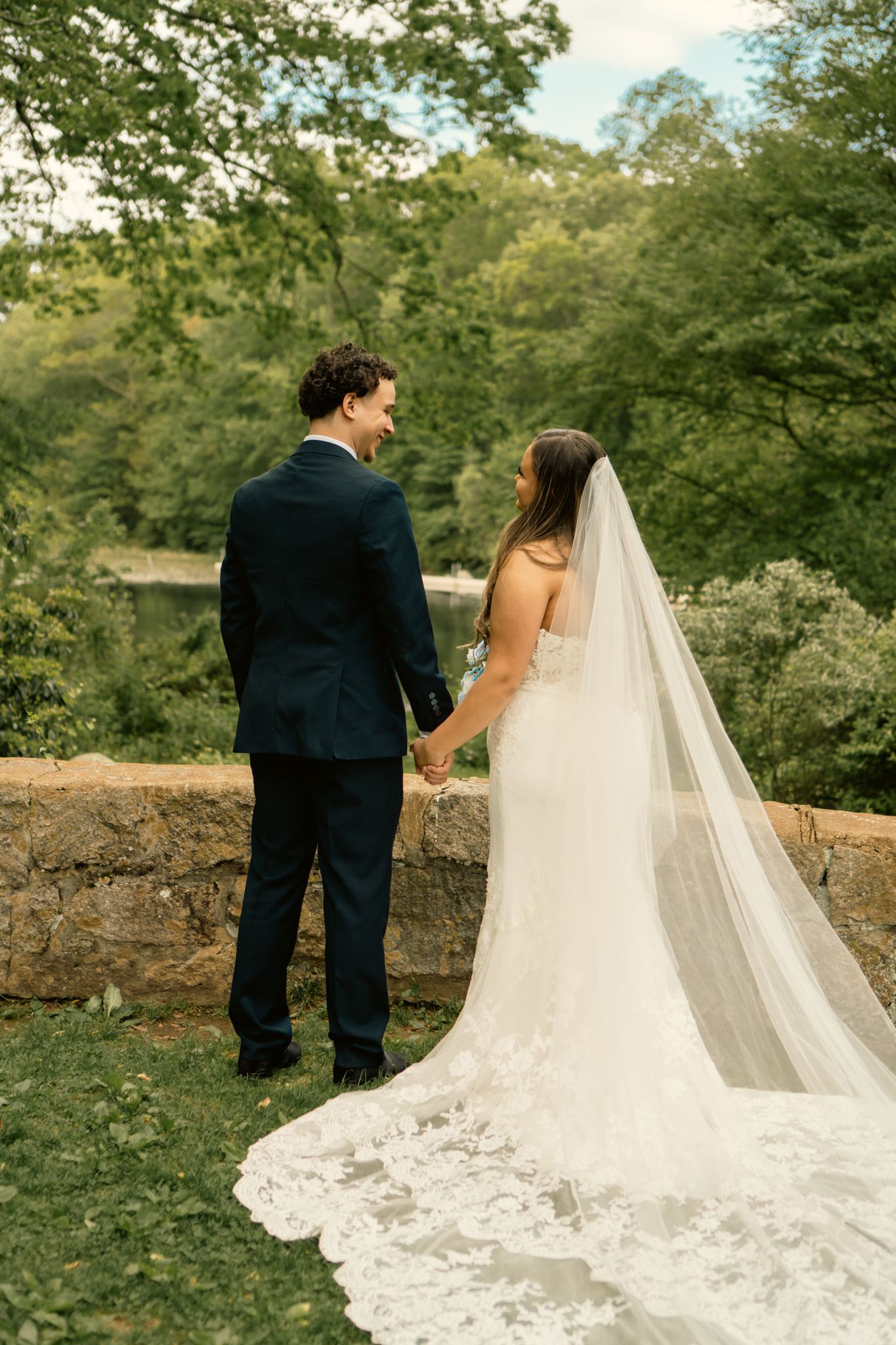 Bride and groom holding hands outdoors, bride wearing a lace gown with long veil.