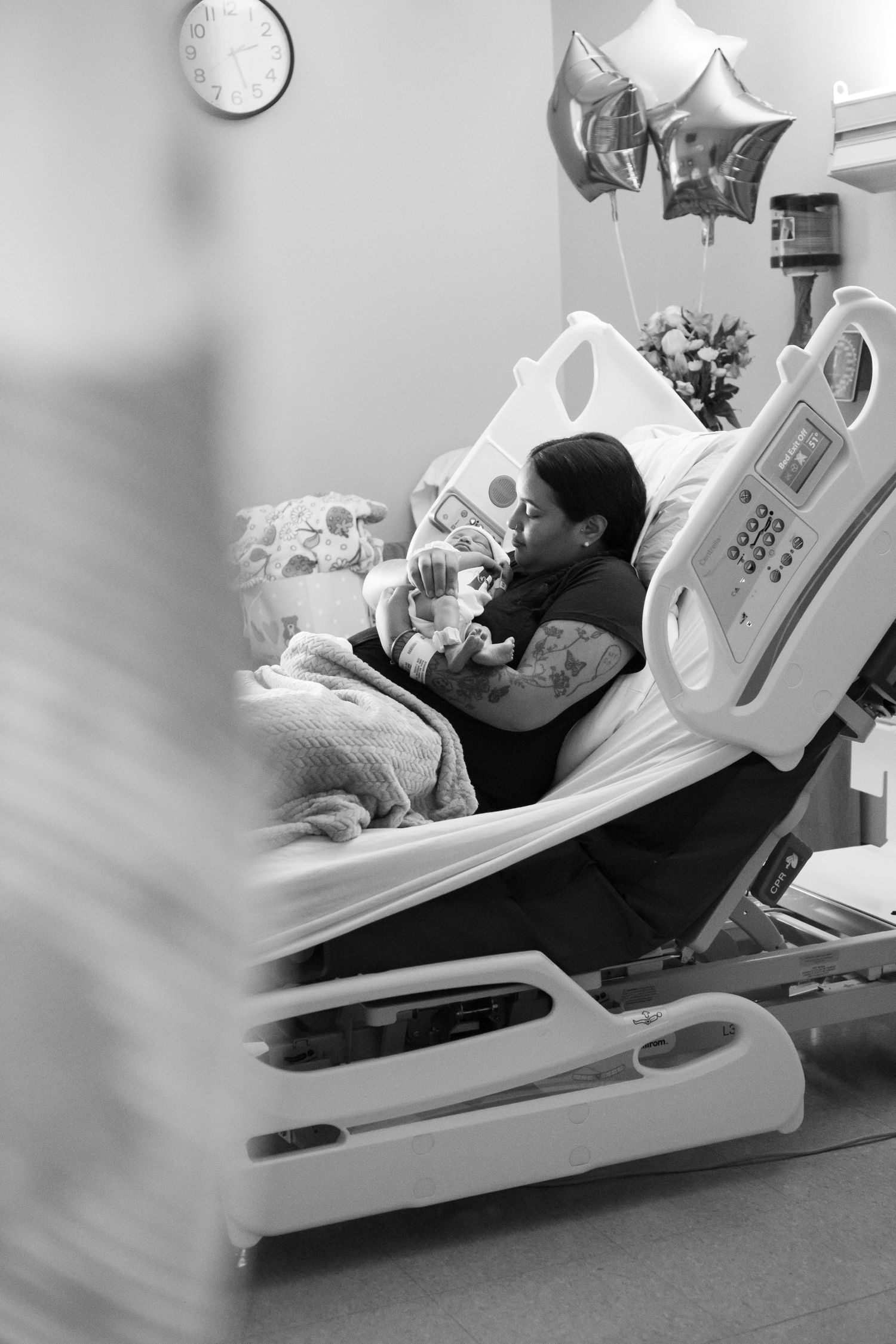 Photo of a woman resting in a hospital bed holding a newborn baby, with balloons and flowers nearby. Lawerence and Memorial New London, CT