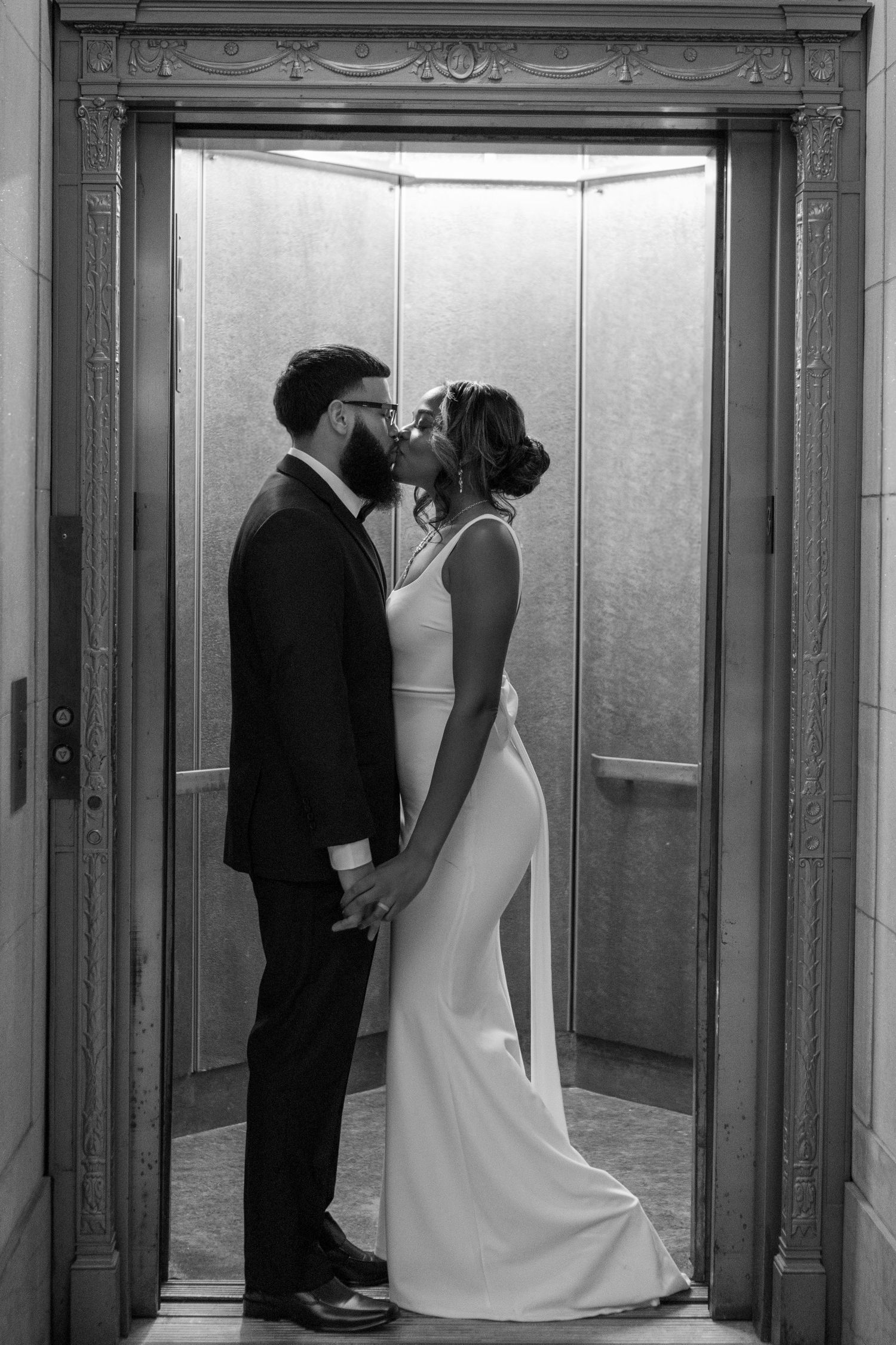 Black and white photo of bride and groom kissing in an ornate elevator.