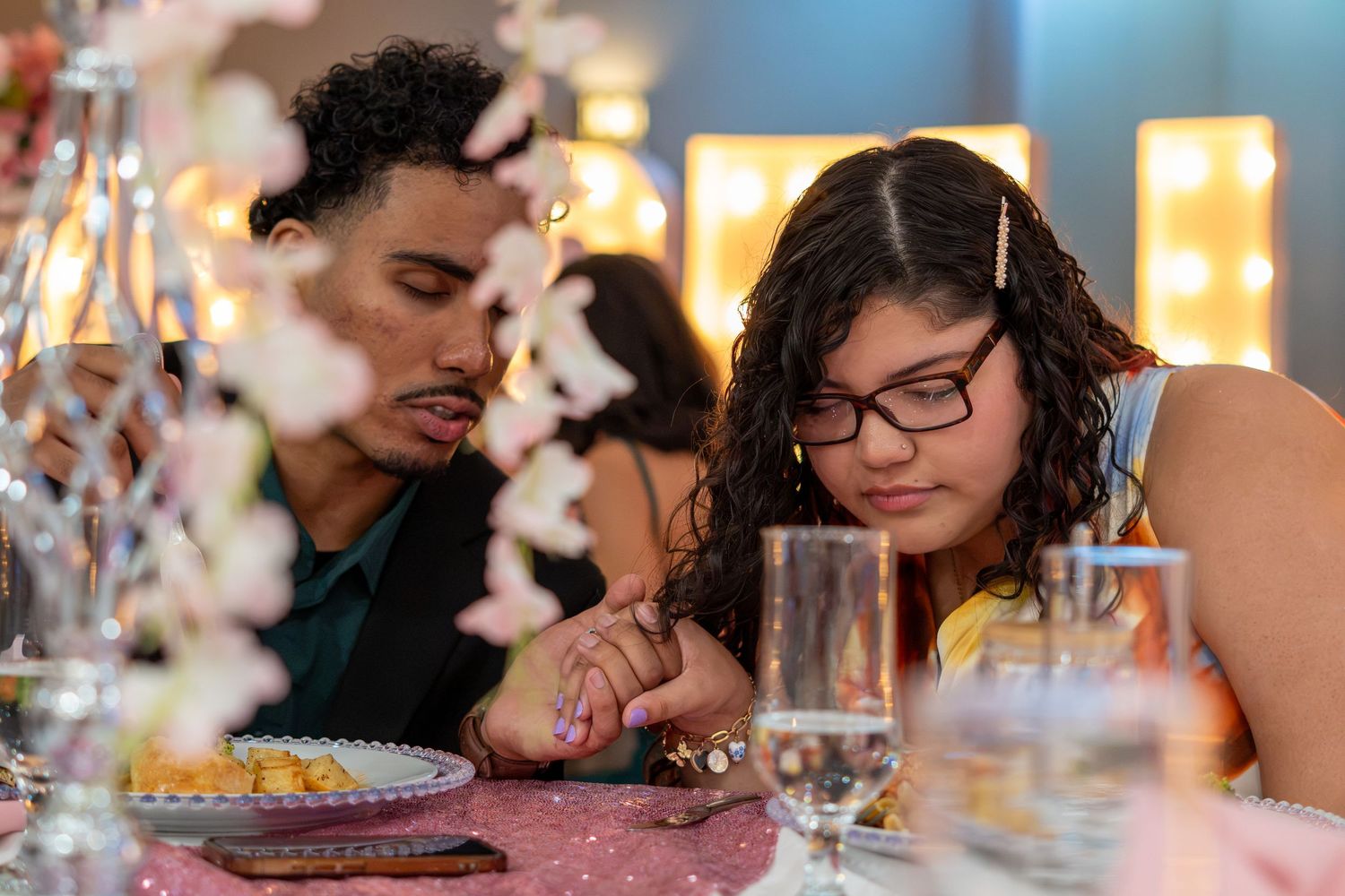 A young couple holds hands at an elegant dinner table decorated with flowers and glowing lights. Sweet 16!