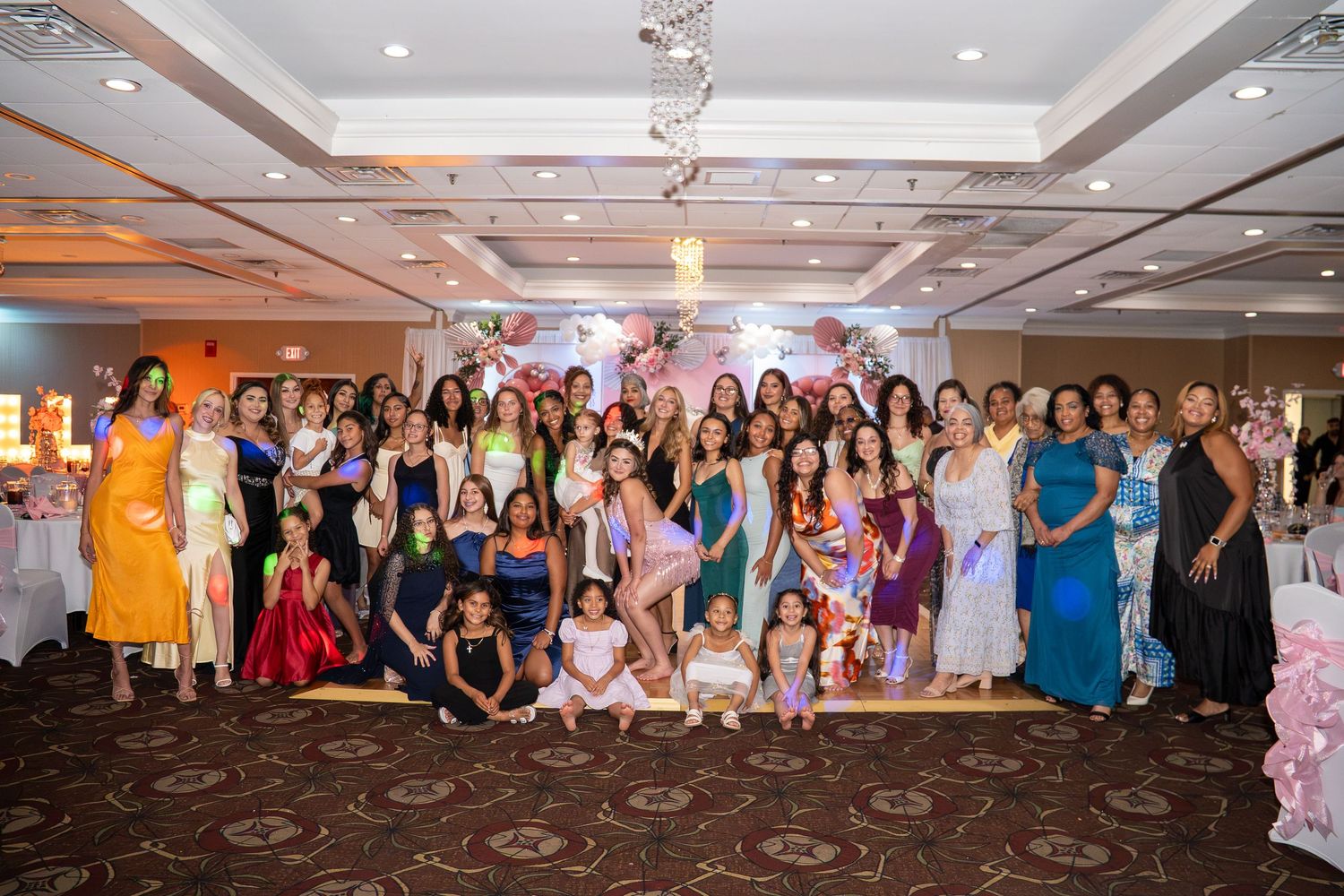 Large group of elegantly dressed women posing together in a decorated banquet hall at a formal pageant event. Sweet 16!