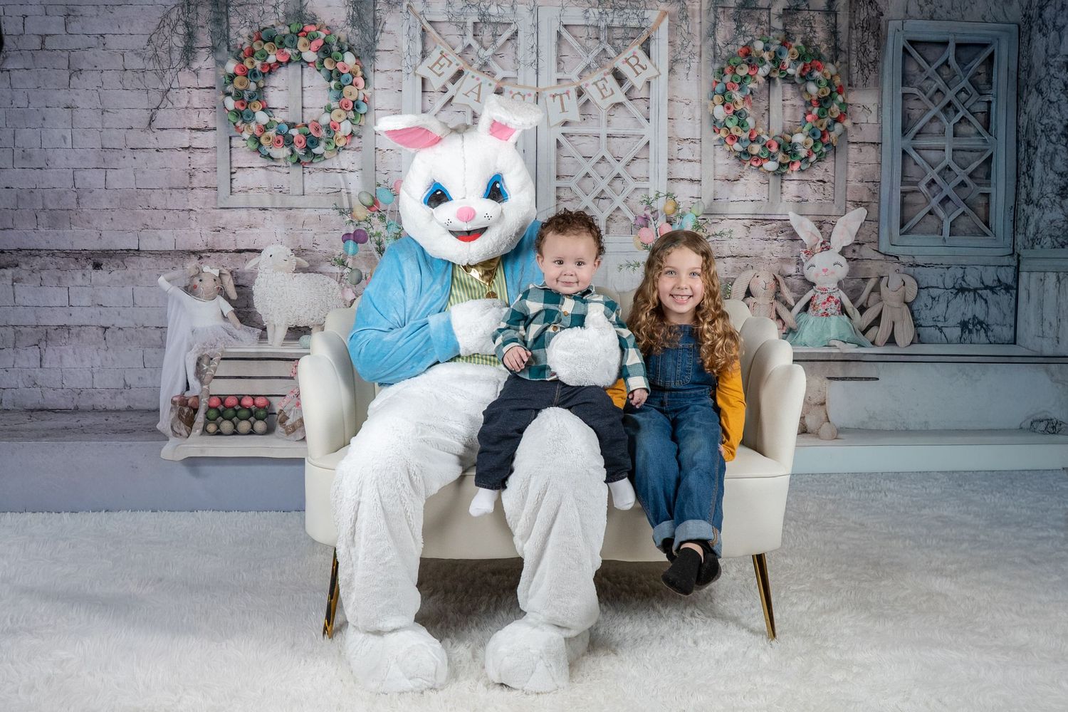 Two children posing with Easter Bunny mascot on white chair with festive backdrop.