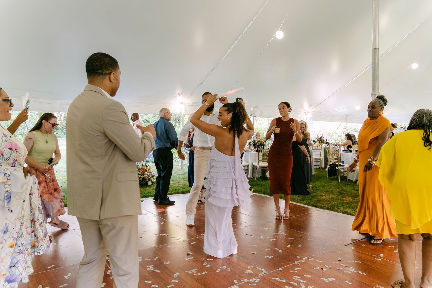 Guests dancing joyfully under a white tent at an outdoor wedding reception on a wooden dance floor.