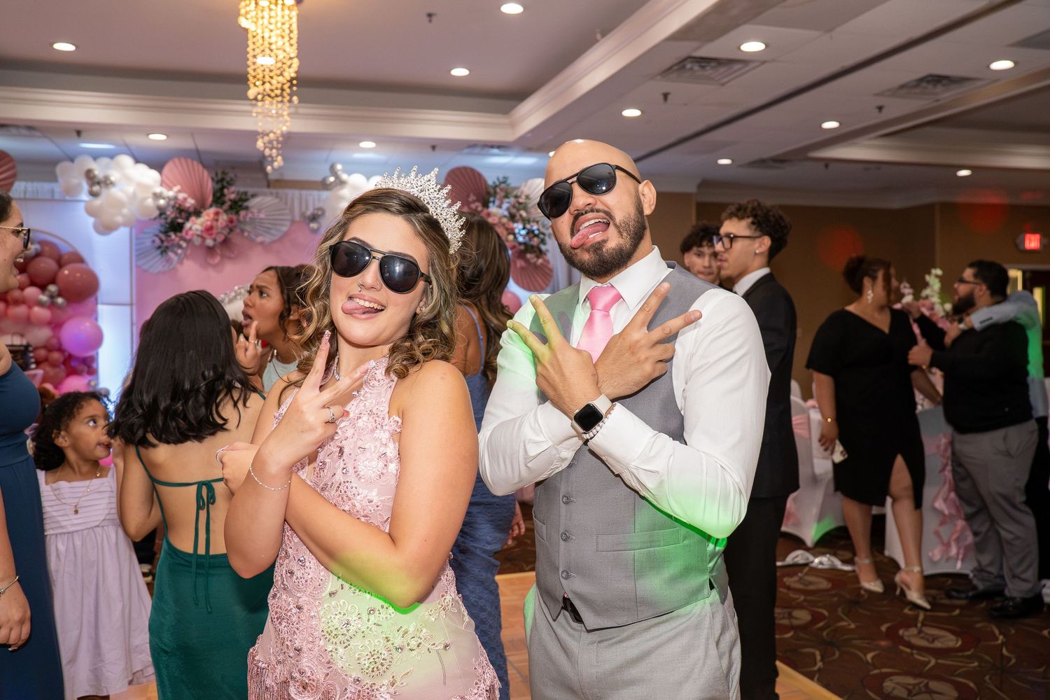 Two guests in sunglasses pose playfully at a festive party with balloon decorations in the background. Sweet 16!