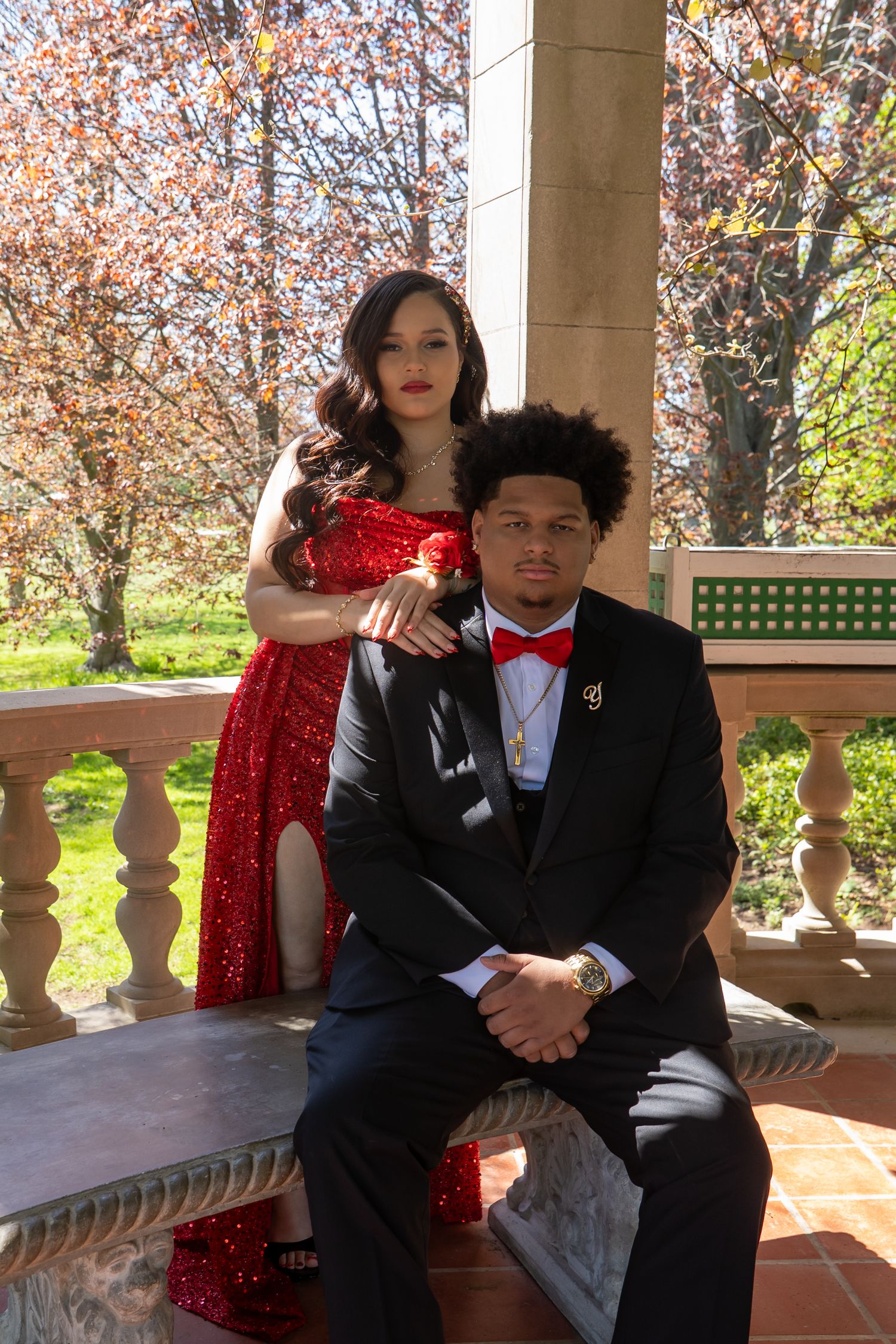 A couple poses for prom photos, woman in red sequin gown and man in black tuxedo with red bow tie.