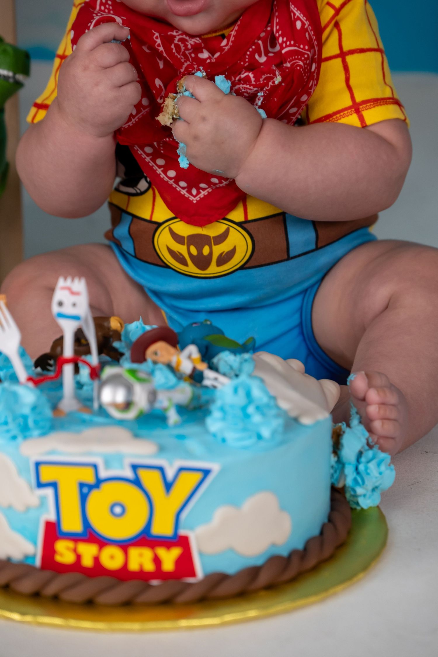Baby in Woody costume sits before a Toy Story themed first birthday cake with character figurines on top. 6month photoshoot