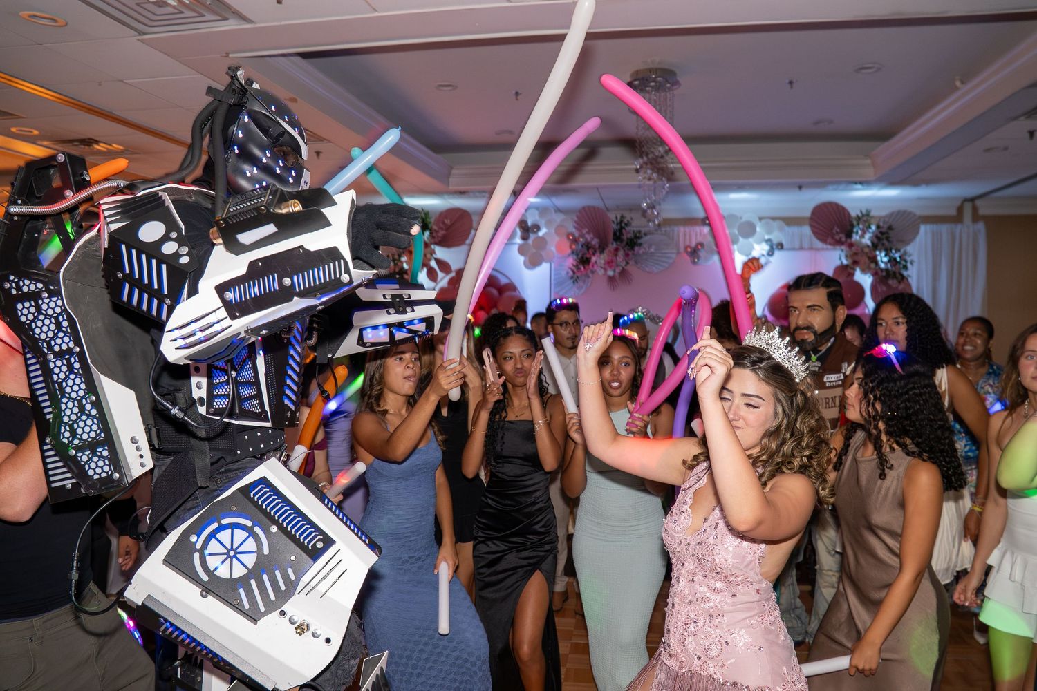 Robot costume entertainer dancing with teens at a colorful party, with glow sticks and balloon decorations. Sweet 16!