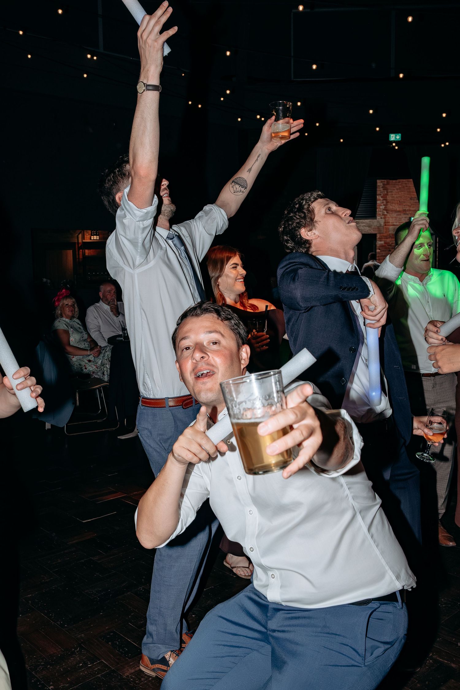 Excited men celebrating at a party, holding beer mugs and glow sticks on a dark dance floor.