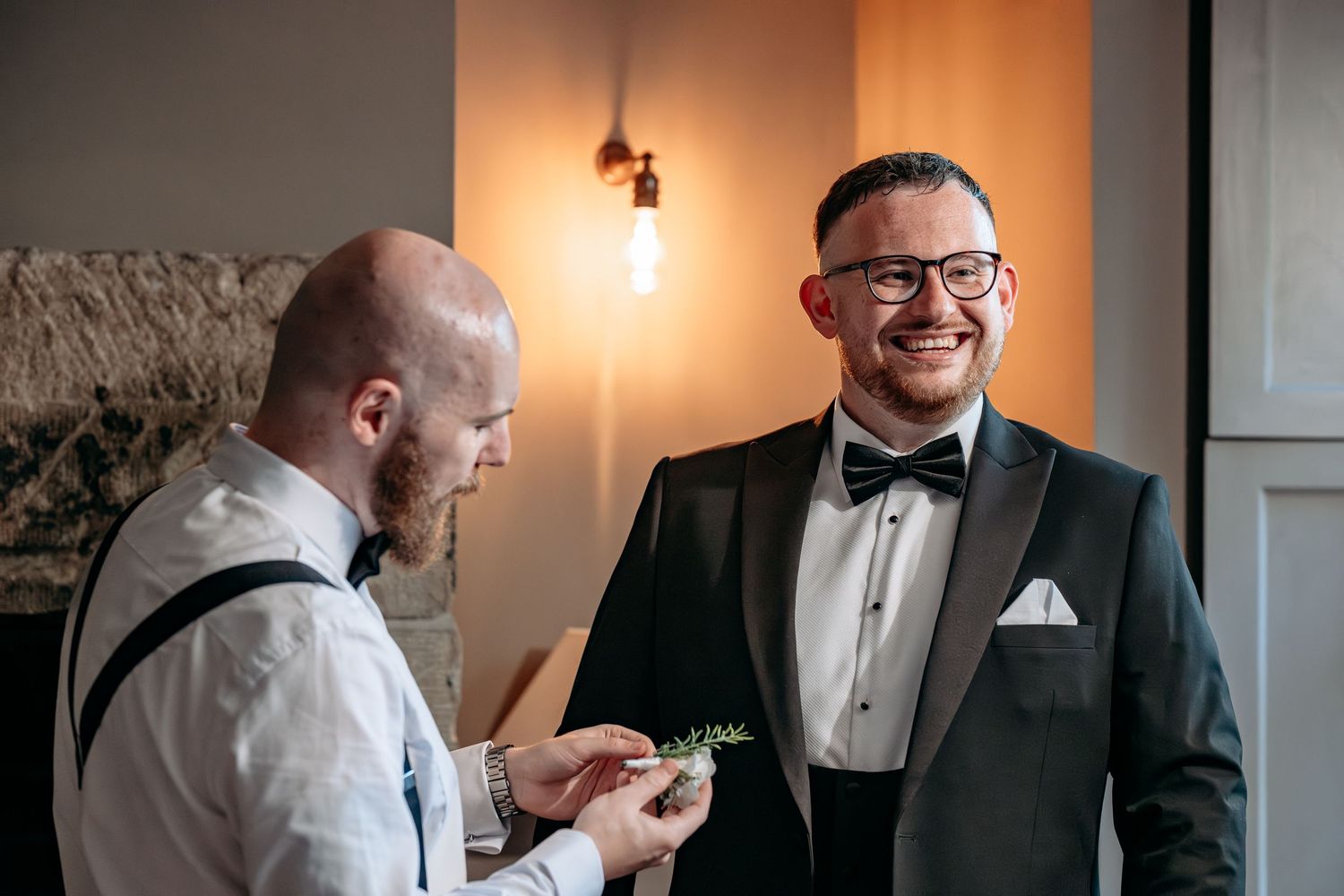 Two grooms sharing a joyful moment before their wedding ceremony, one in a tuxedo with bow tie.