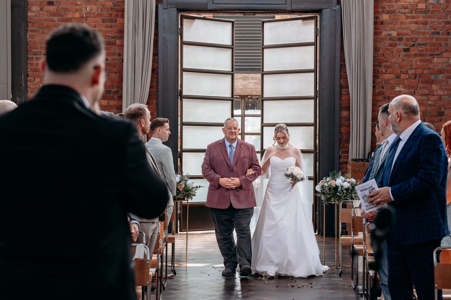 Bride walks down the aisle with her father in a rustic brick venue during a wedding ceremony.