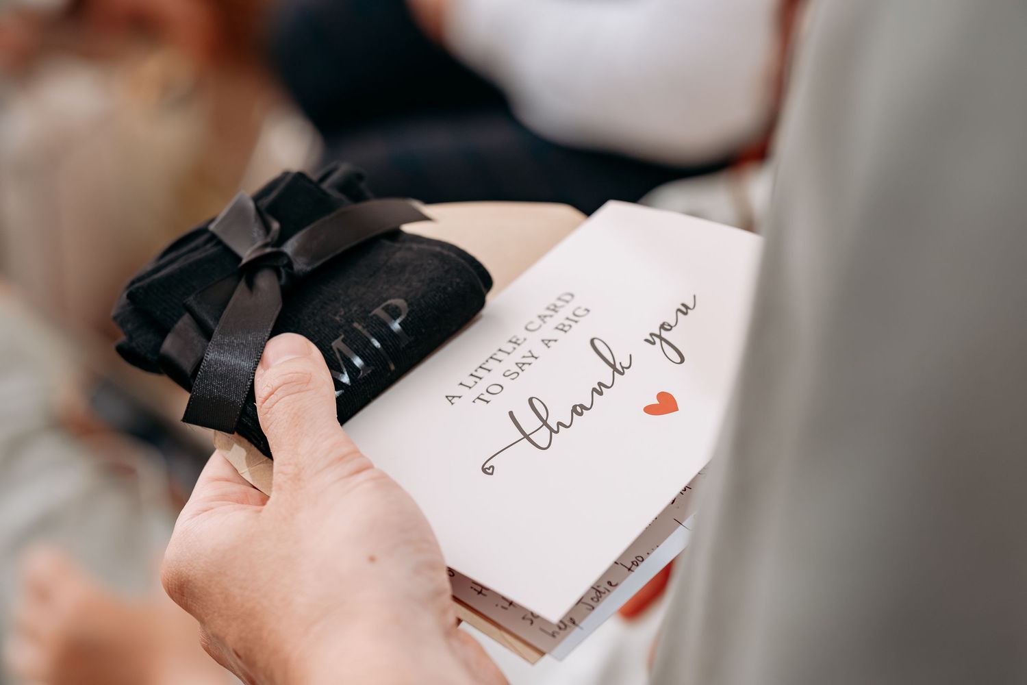Hand holding a thank you card with a black bow gift, perfect for weddings or special occasions.