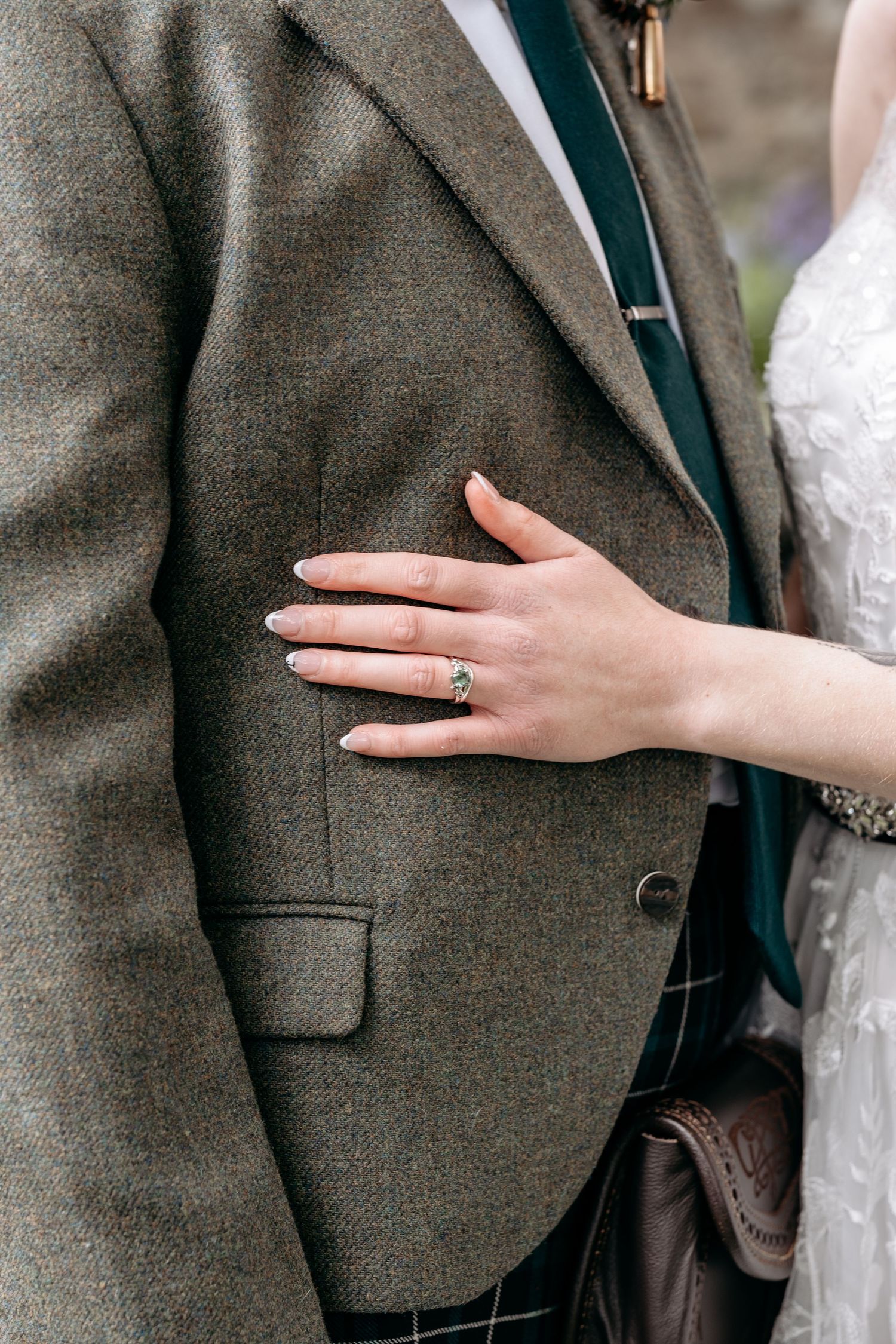 Bride's hand with engagement ring resting on groom's tweed jacket at wedding ceremony.