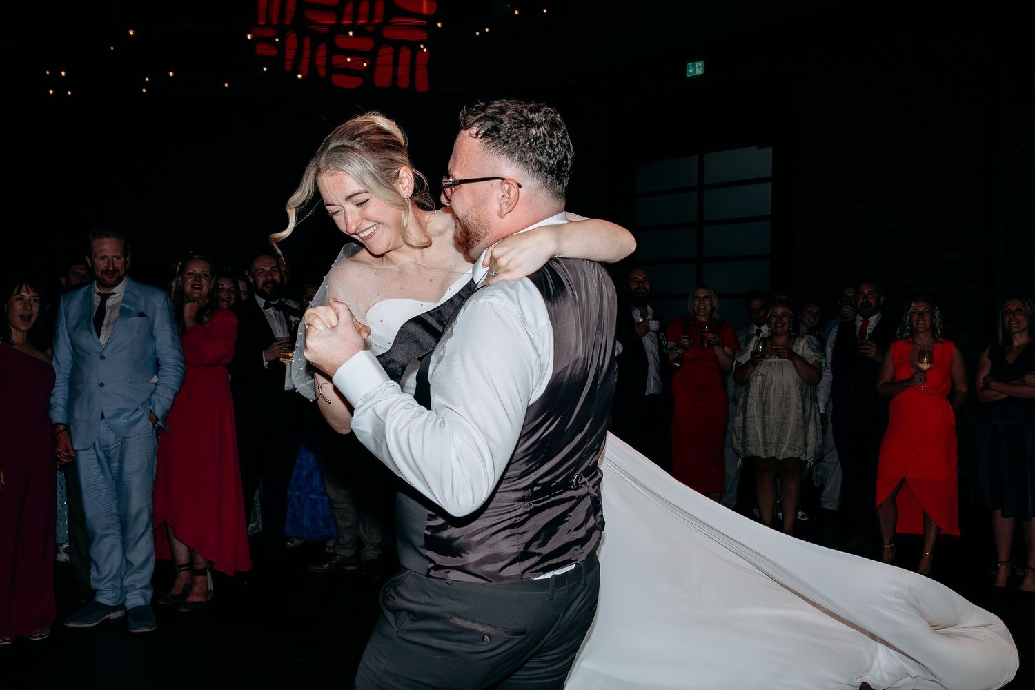 Bride and groom share romantic first dance, groom dipping bride in white wedding gown at elegant reception.