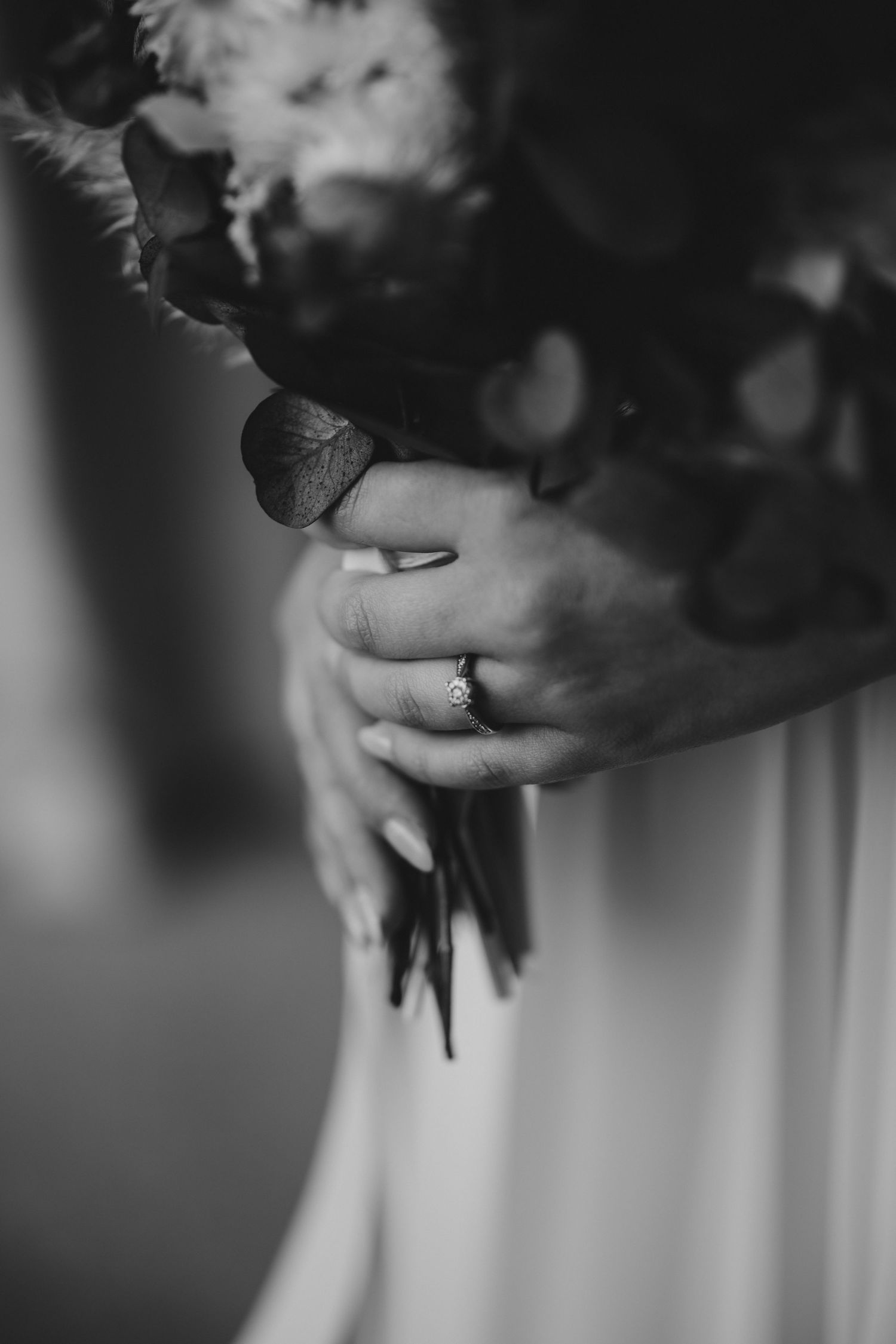 Black and white close-up of bride holding a wedding bouquet with an engagement ring visible.