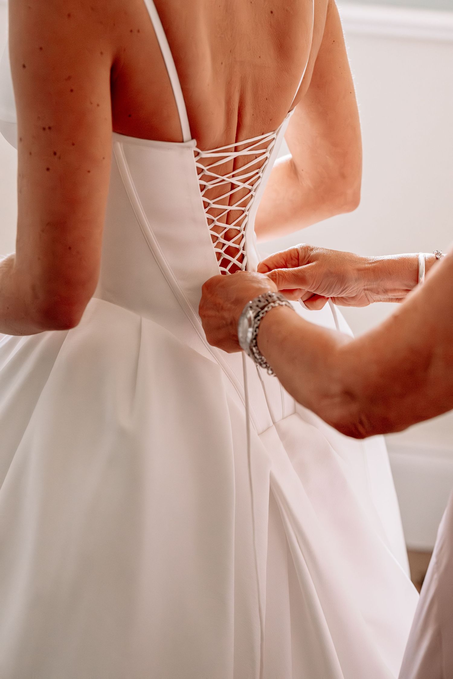 Helper lacing up the back of a white bridal corset wedding gown, close-up detail shot.