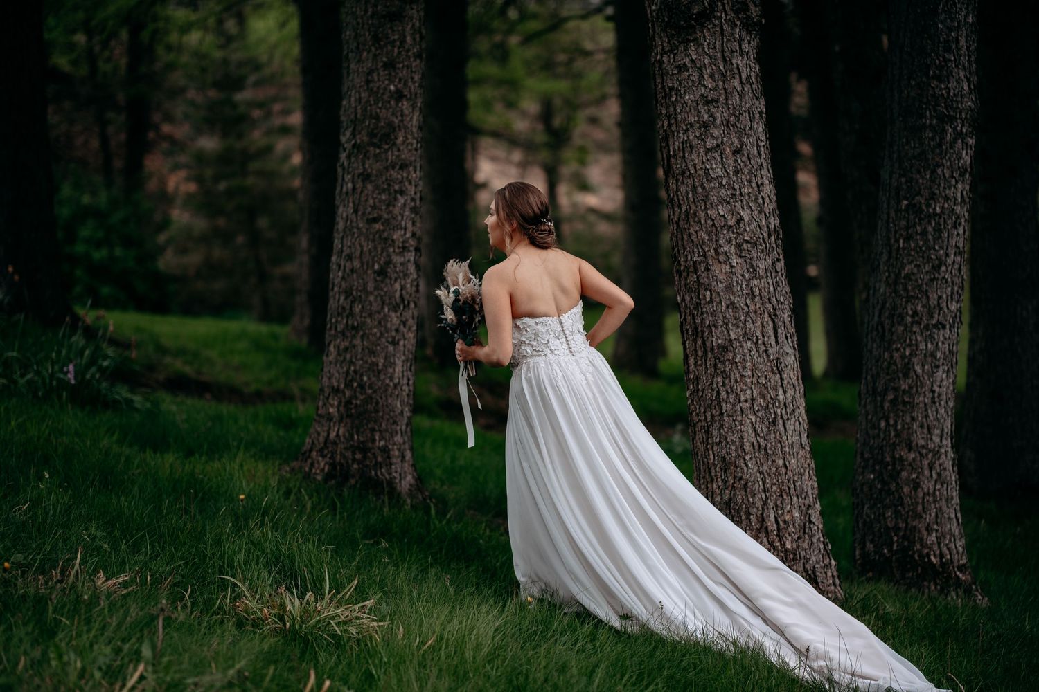 Bride in elegant white gown with long train walking through a serene forest setting.