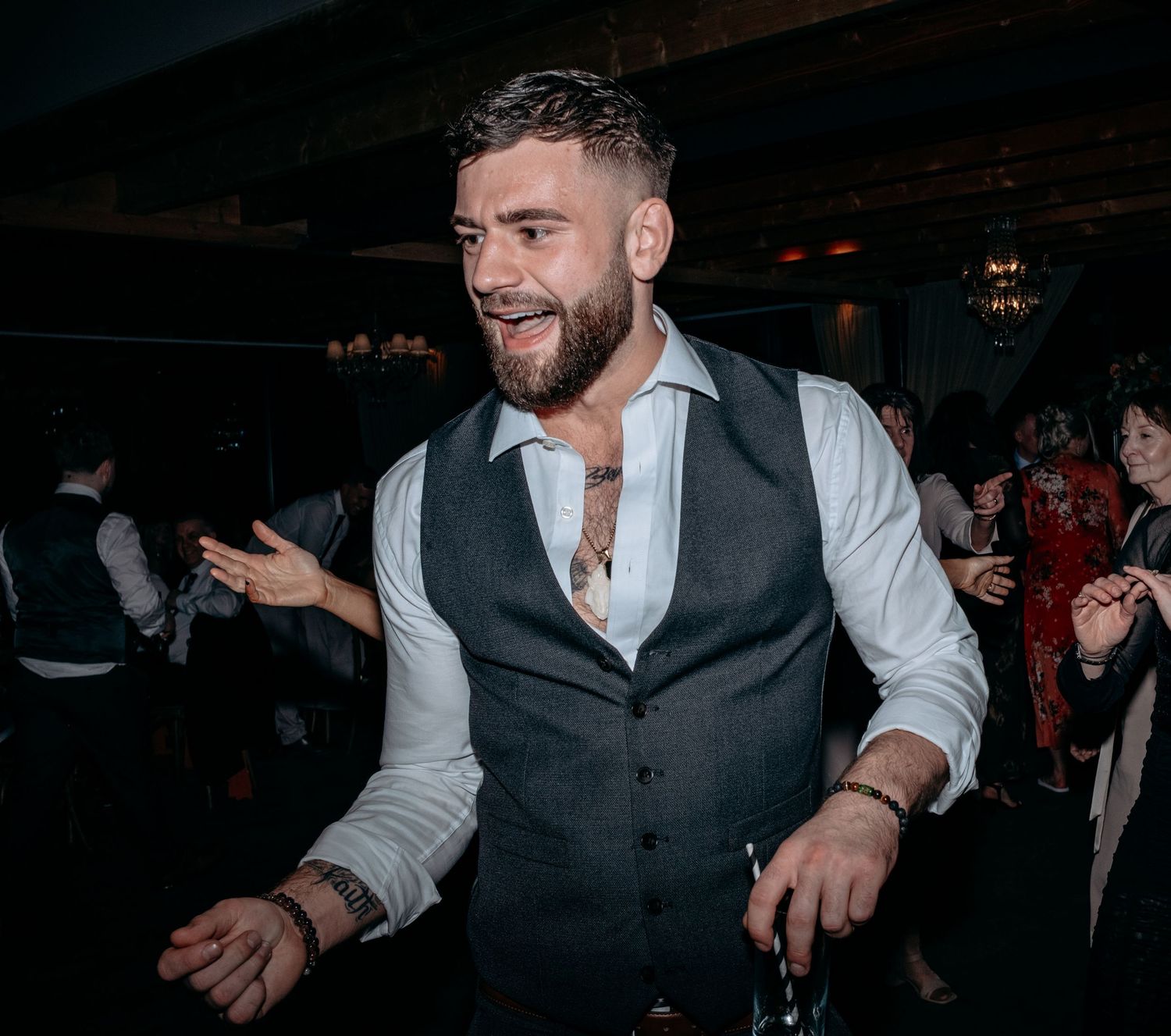A cheerful bearded man in a gray vest and white shirt dancing at a lively evening party event.