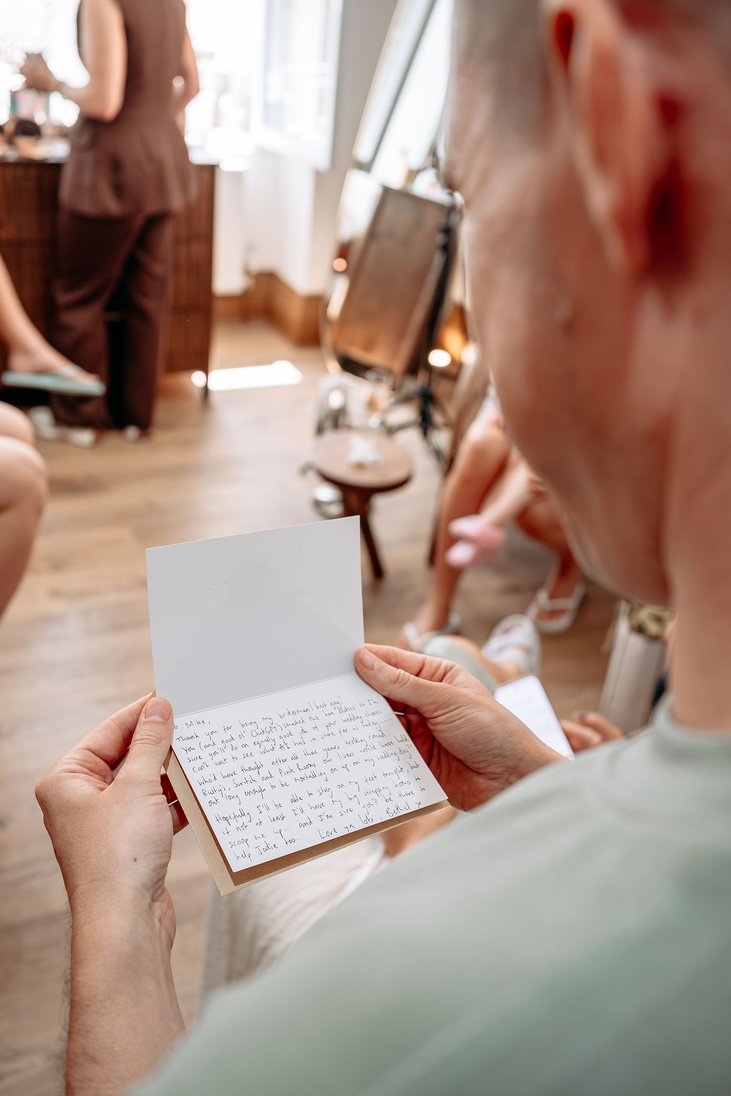 Man reading a handwritten letter card in a bright indoor setting with people in the background.
