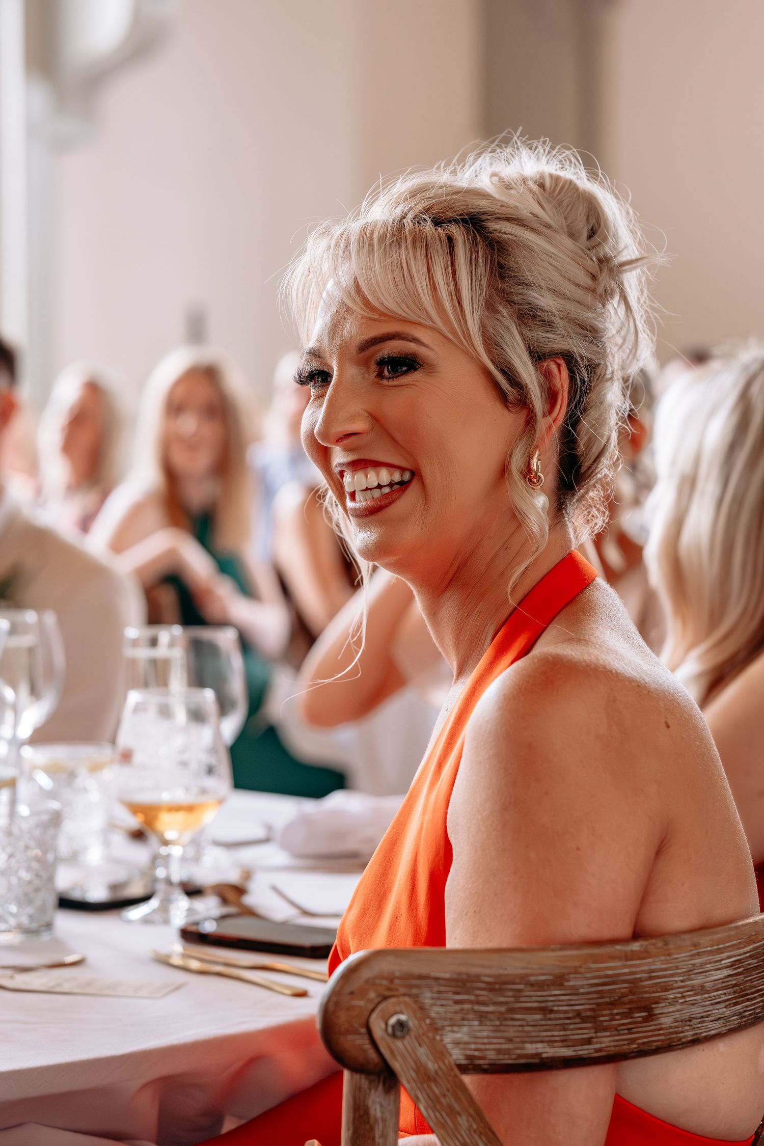 Smiling blonde woman in red halter dress seated at elegant dining table during formal event or wedding reception.