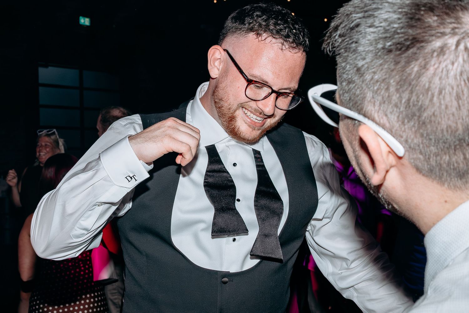 Man in vest and bow tie adjusting his outfit at a formal party event.