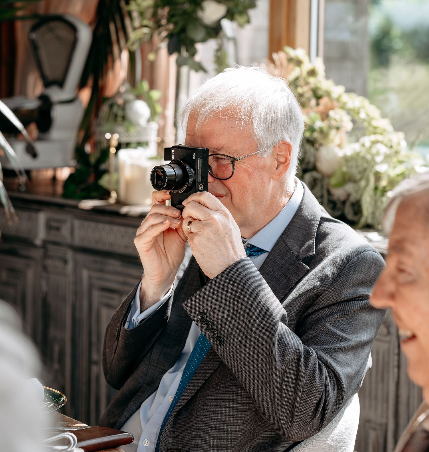 Elderly man with gray hair and glasses photographing with a vintage camera at an elegant wedding reception.