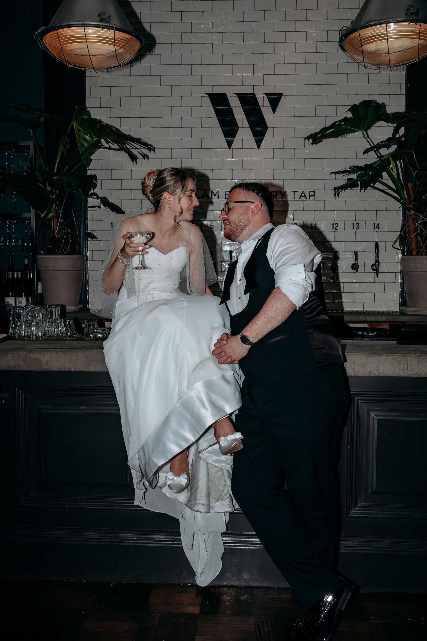 Bride and groom sitting together at a bar, sharing a romantic moment with cocktails at their wedding reception.