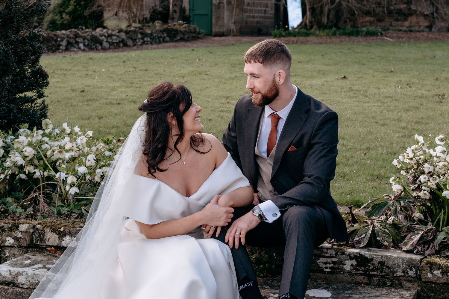 Bride and groom sitting together on stone steps in a lush garden during their wedding day.