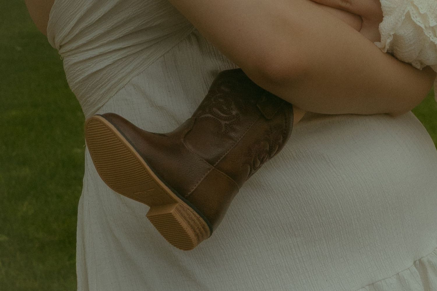 Close-up of brown leather cowboy boots worn with a white dress, perfect for rustic wedding or country style.