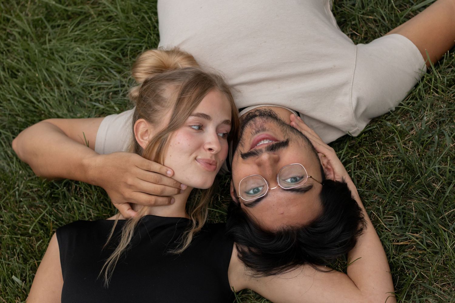 Couple lying together on green grass during an intimate moment.