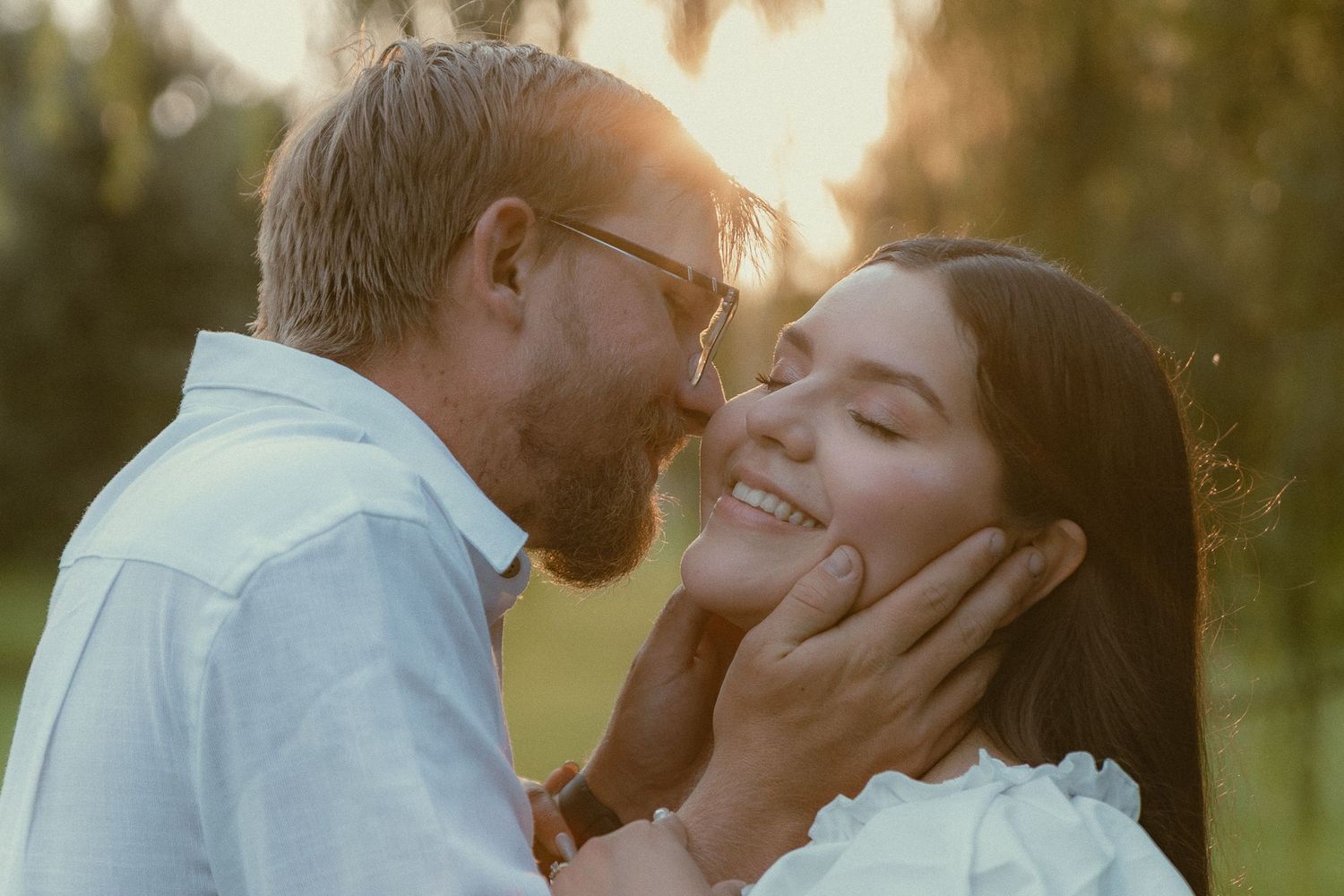 Romantic couple sharing a tender moment outdoors at golden hour, man gently holding woman's face as she smiles.