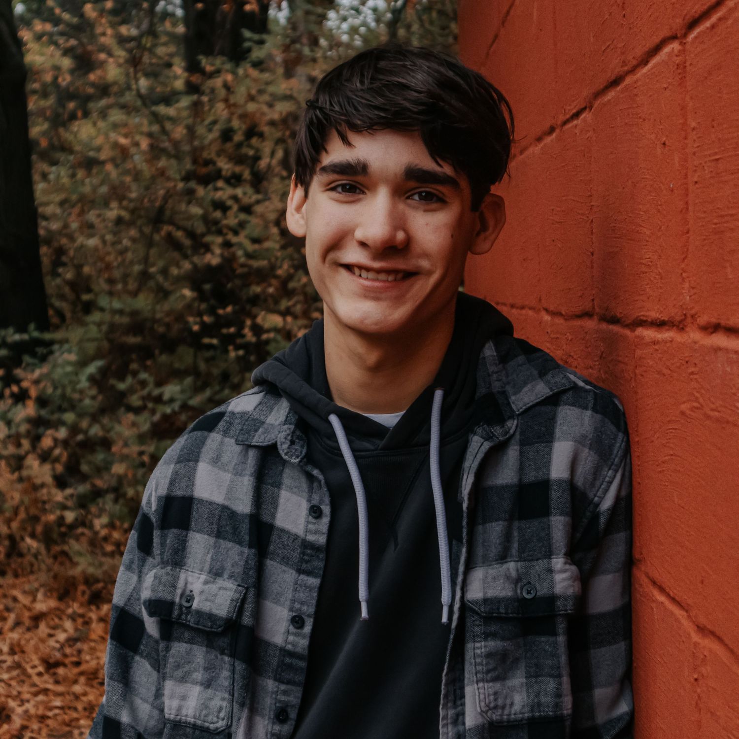 Portrait against red brick wall showing casual autumn style with plaid flannel and hoodie.