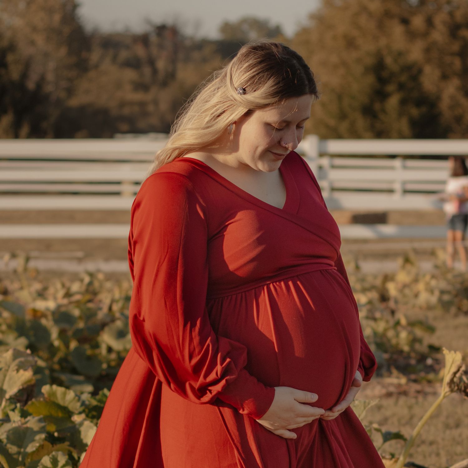Maternity photo in flowing red dress during golden hour in autumn field setting.