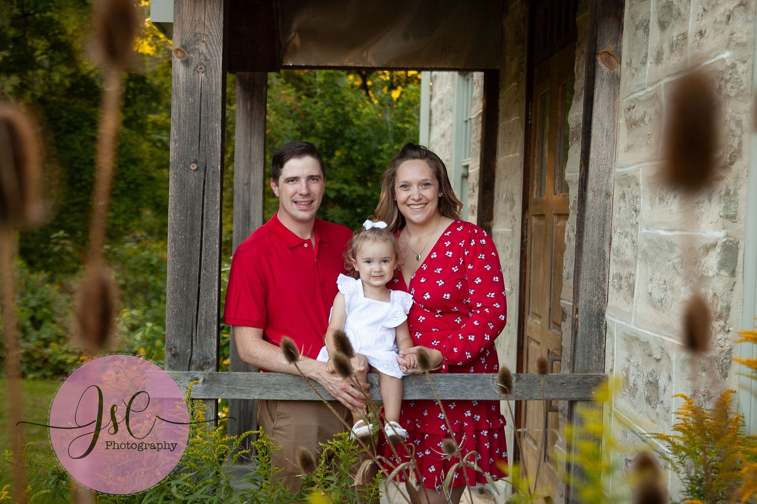 A group of people wearing red and white outfits pose together under a rustic stone and wood structure outdoors.