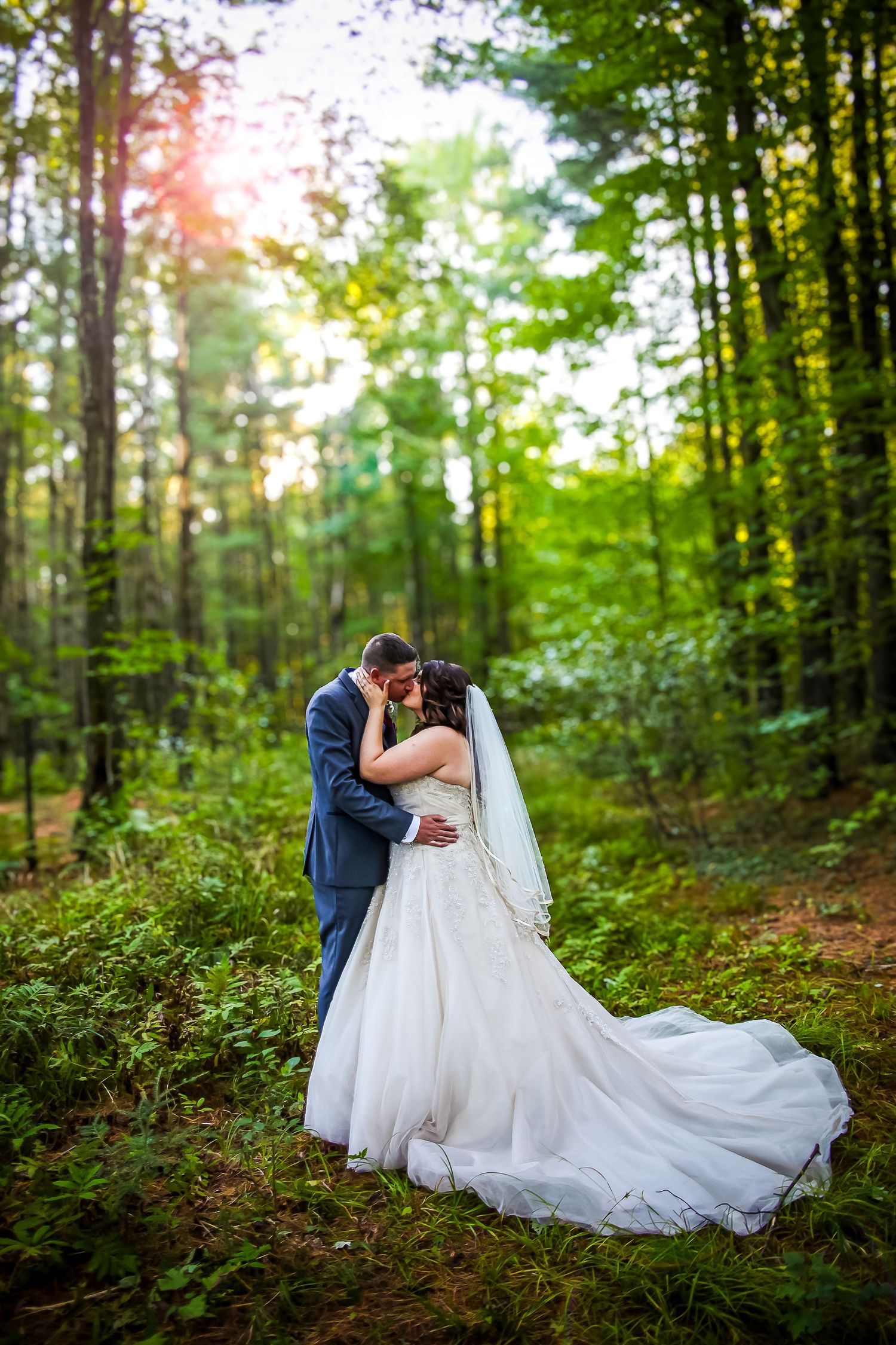 A romantic wedding couple shares an intimate moment in a lush forest setting with flowing white dress and natural lighting.