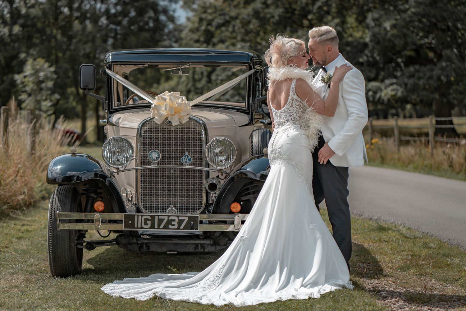 Wedding couple posing near vintage cars in countryside setting.