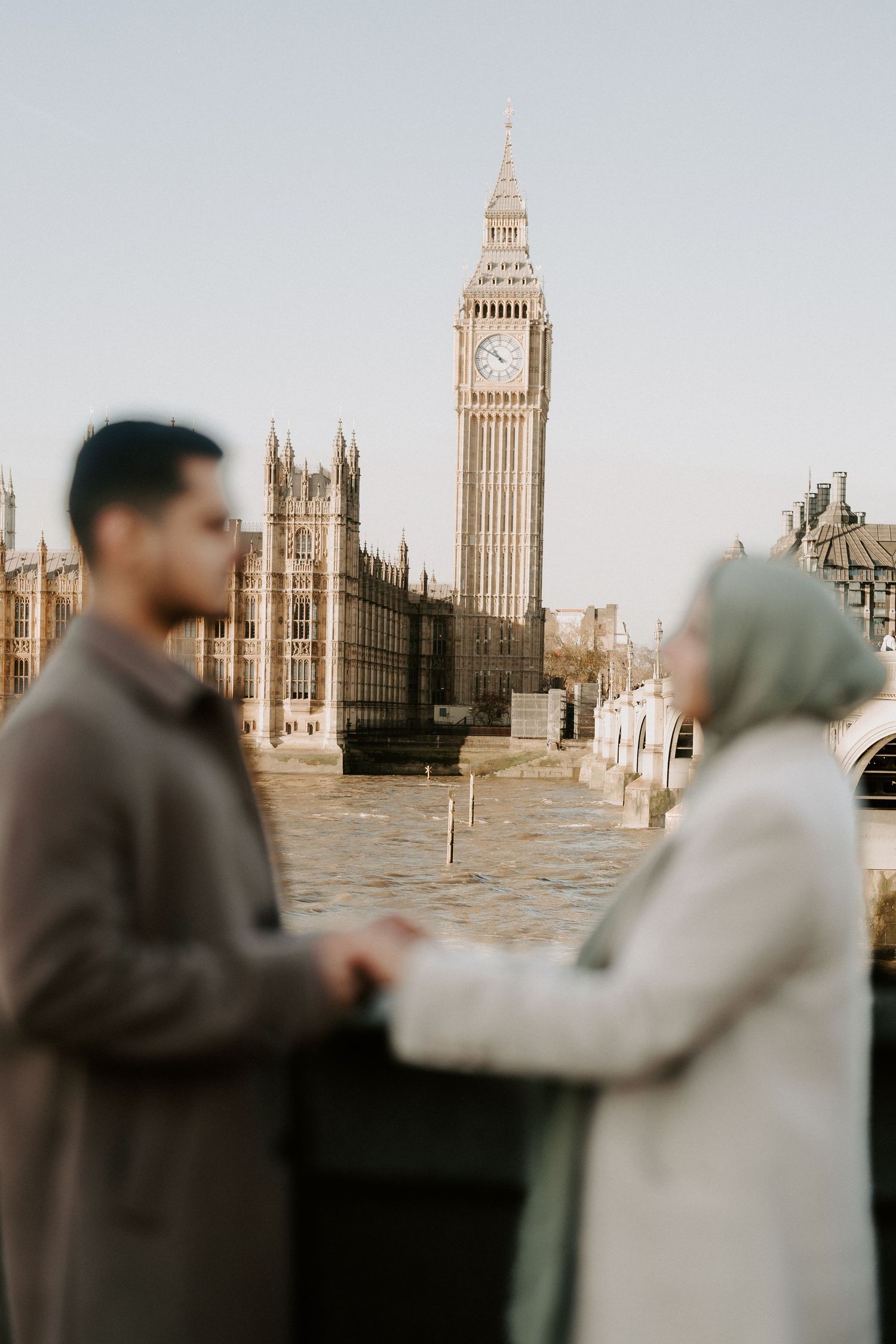 A couple holds hands on a bridge with Big Ben and the Houses of Parliament in the background in London.
