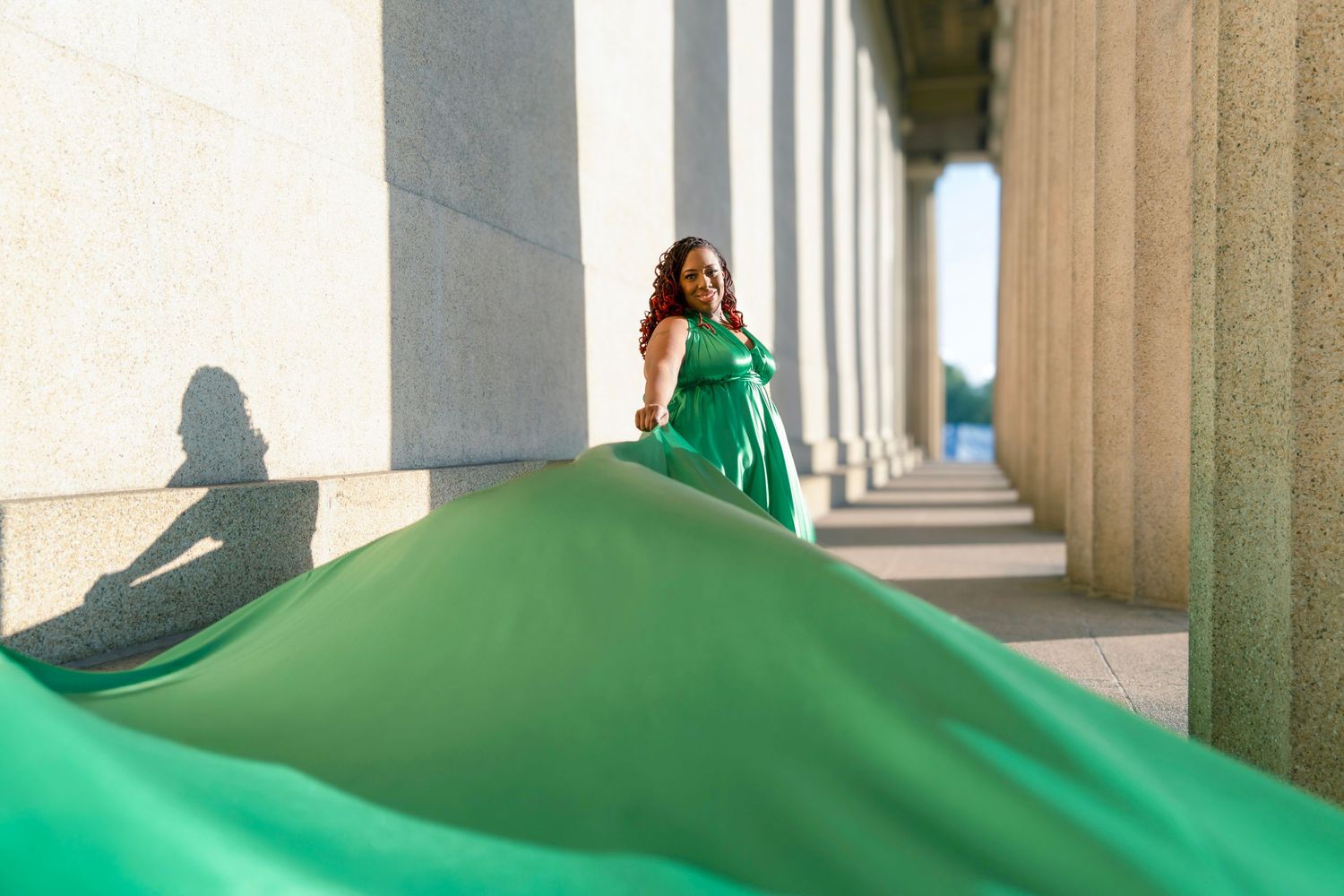 Woman in bright green jumpsuit poses elegantly in a columned hallway with arched architecture.