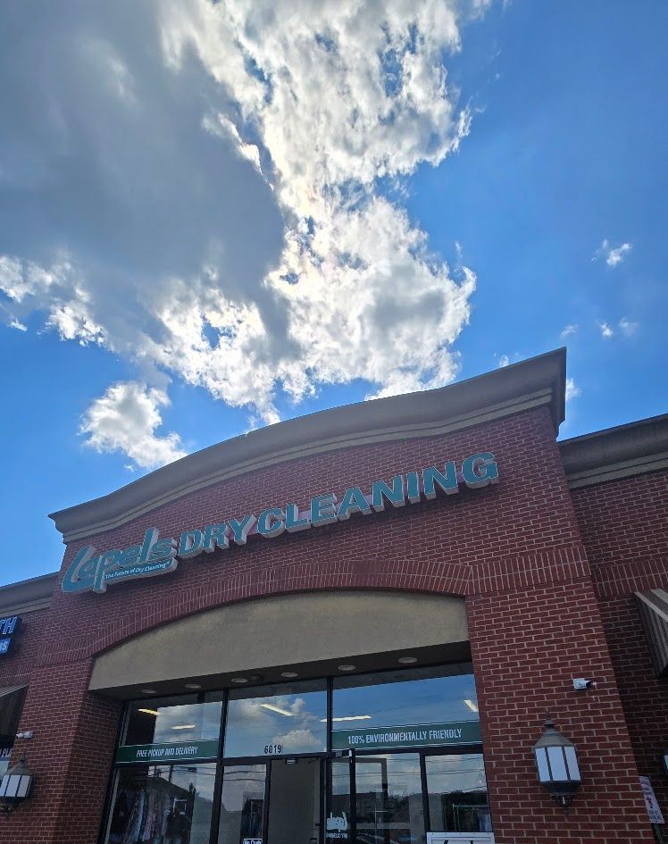 Commercial brick building with glass storefronts and signage under a bright blue sky with puffy white clouds.