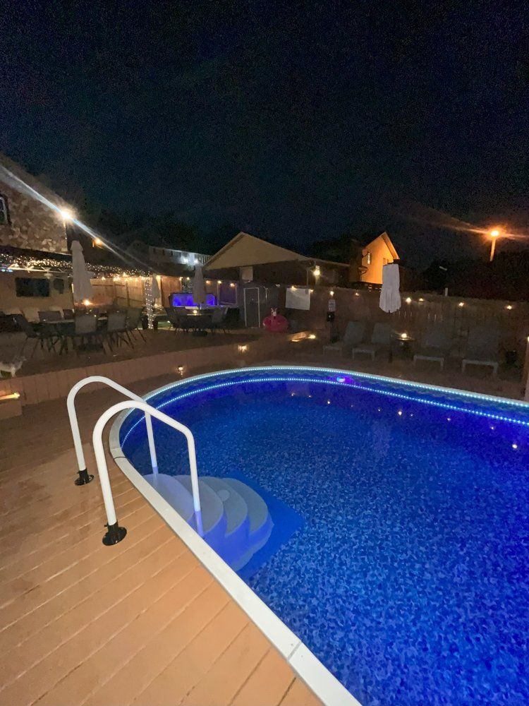 Above-ground swimming pool illuminated with blue LED lights at night featuring a curved handrail and deck.