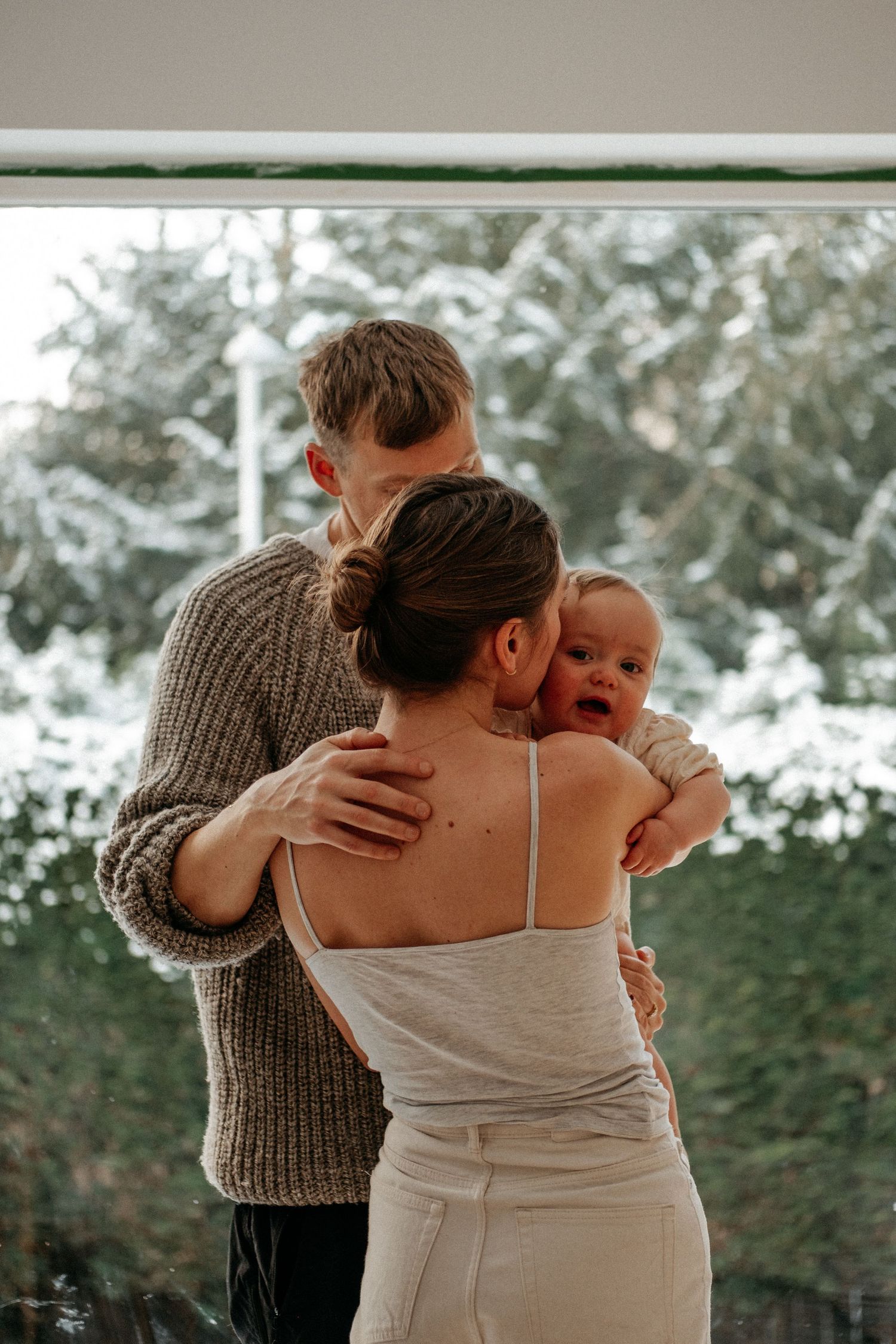 A family of three standing in front of a window holding each other in a tight embrace during a family photoshoot in Gateshead